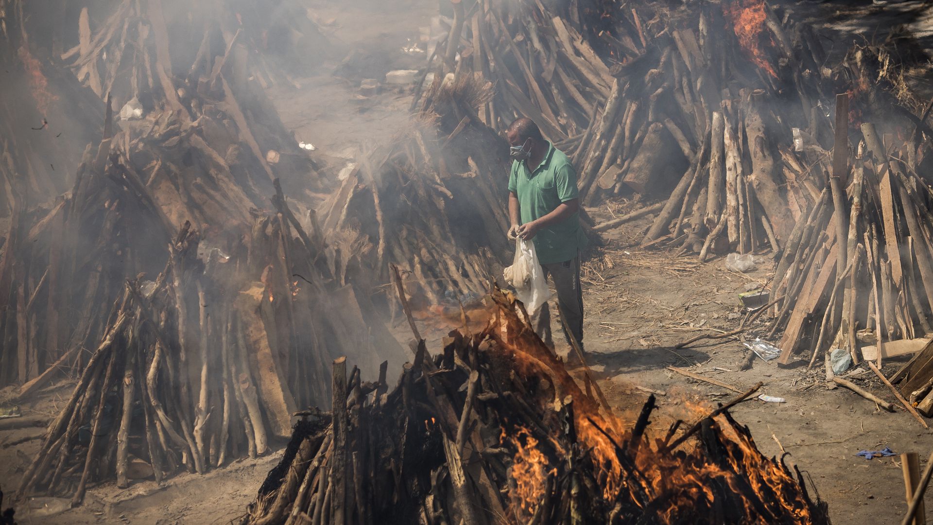 A man performs the last rites of his relative who died of Covid-19 as other funeral pyres are seen burning during a mass cremation held at a crematorium on April 24, 2021 in New Delhi, India.