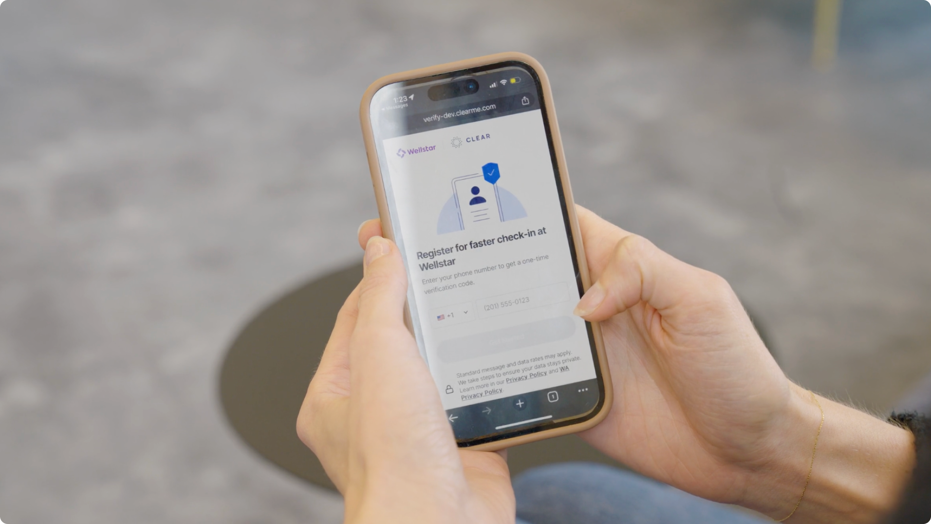 Person holding smartphone with a beige case displaying Wellstar and CLEAR logos and a sign-up page for faster check-in at Wellstar on the screen.