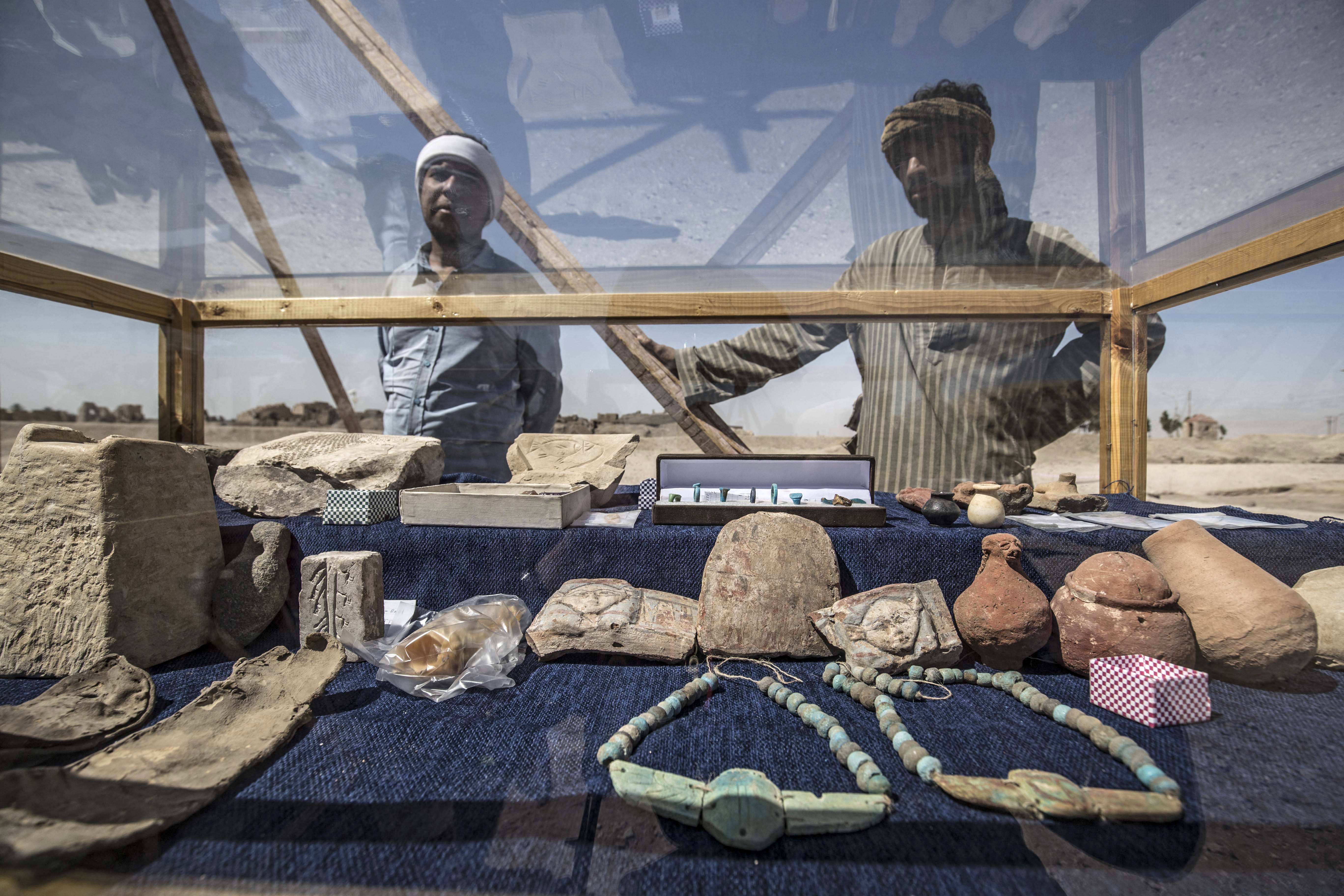 Workers standing next to a display of artifacts uncovered at the archaeological site of a 3000 year old city