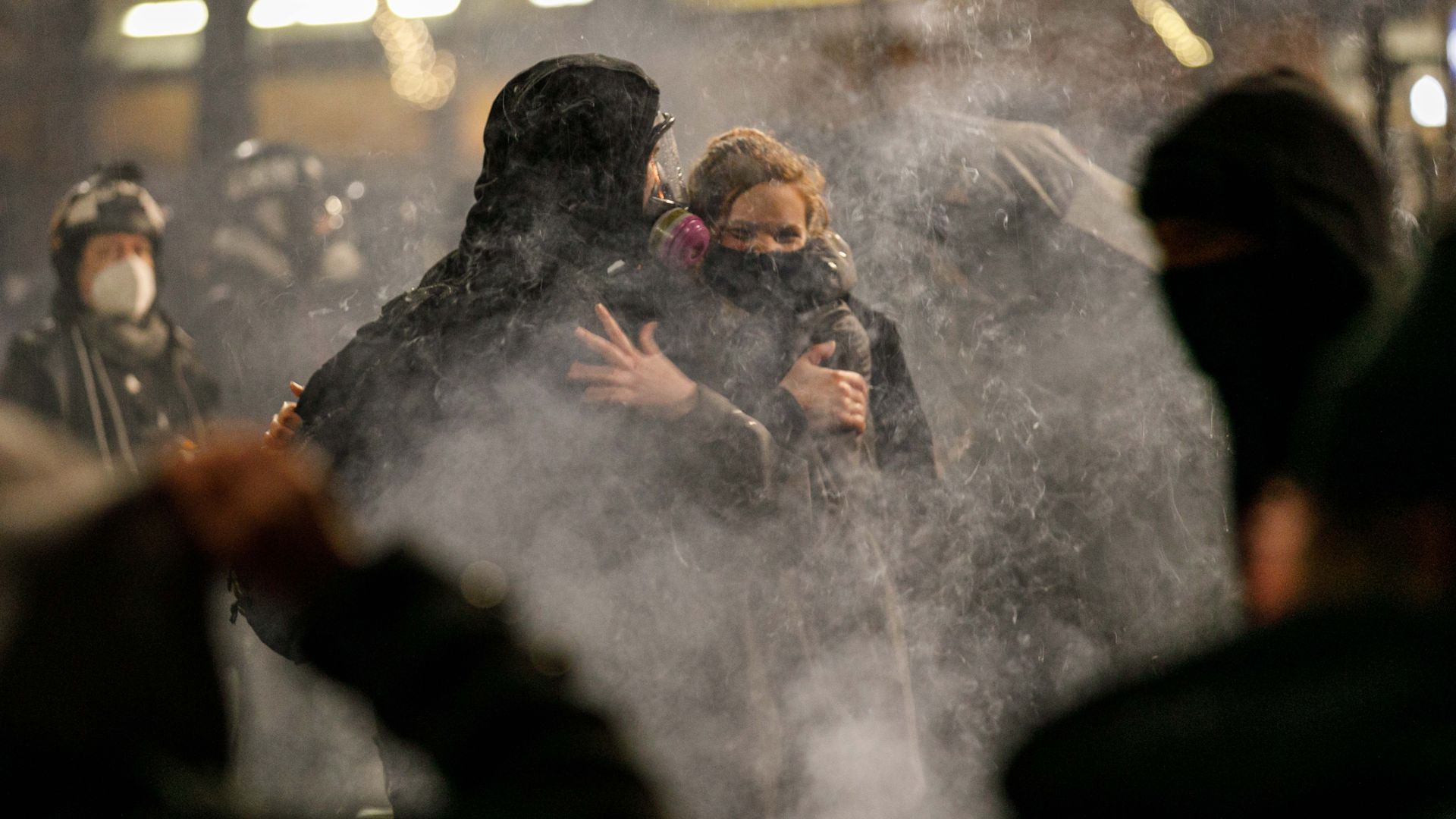 Two people wearing gas masks in a cloud of tear gas during clashes with police. 