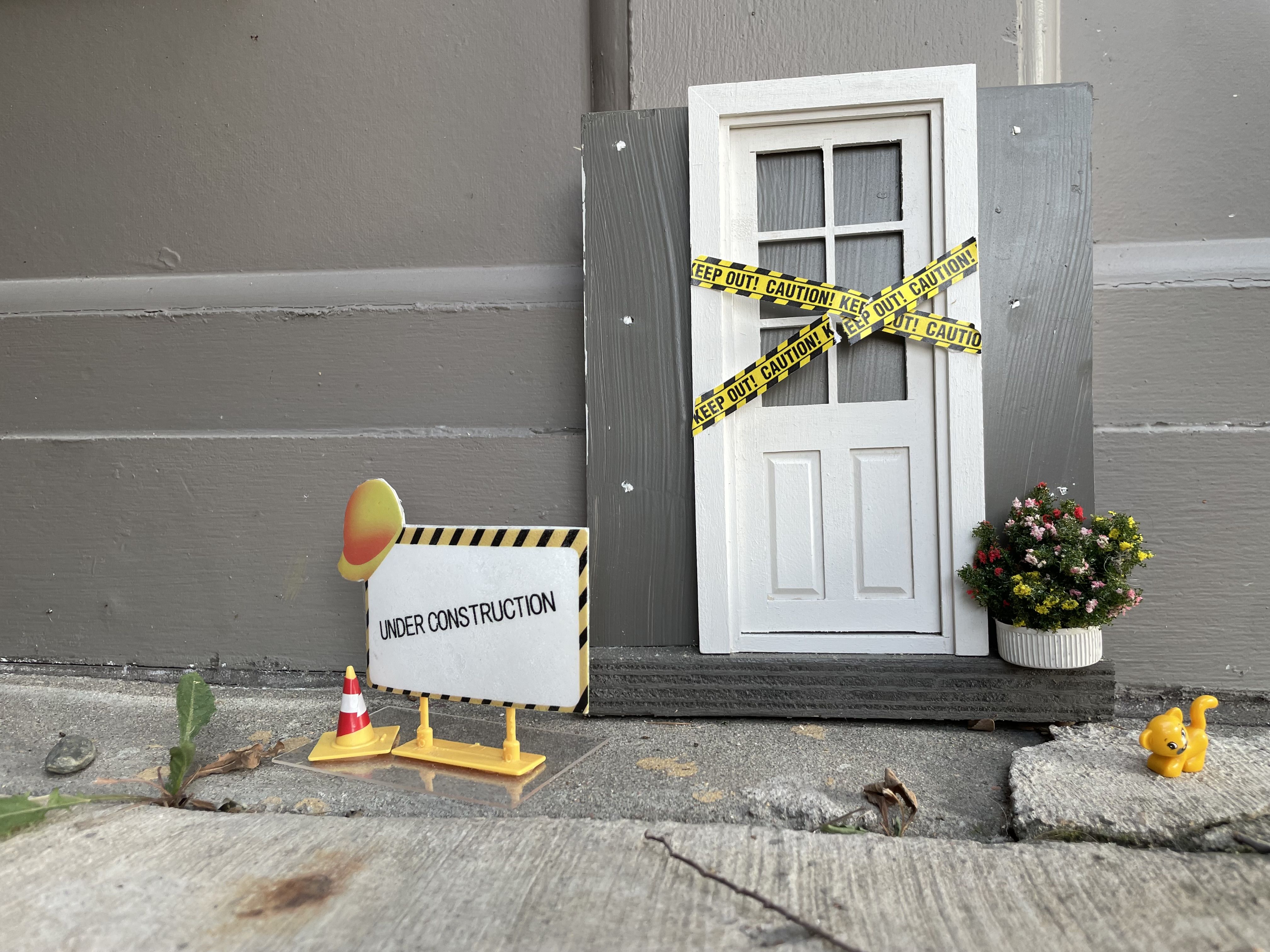 A tiny door with tiny caution tape and an under construction sign