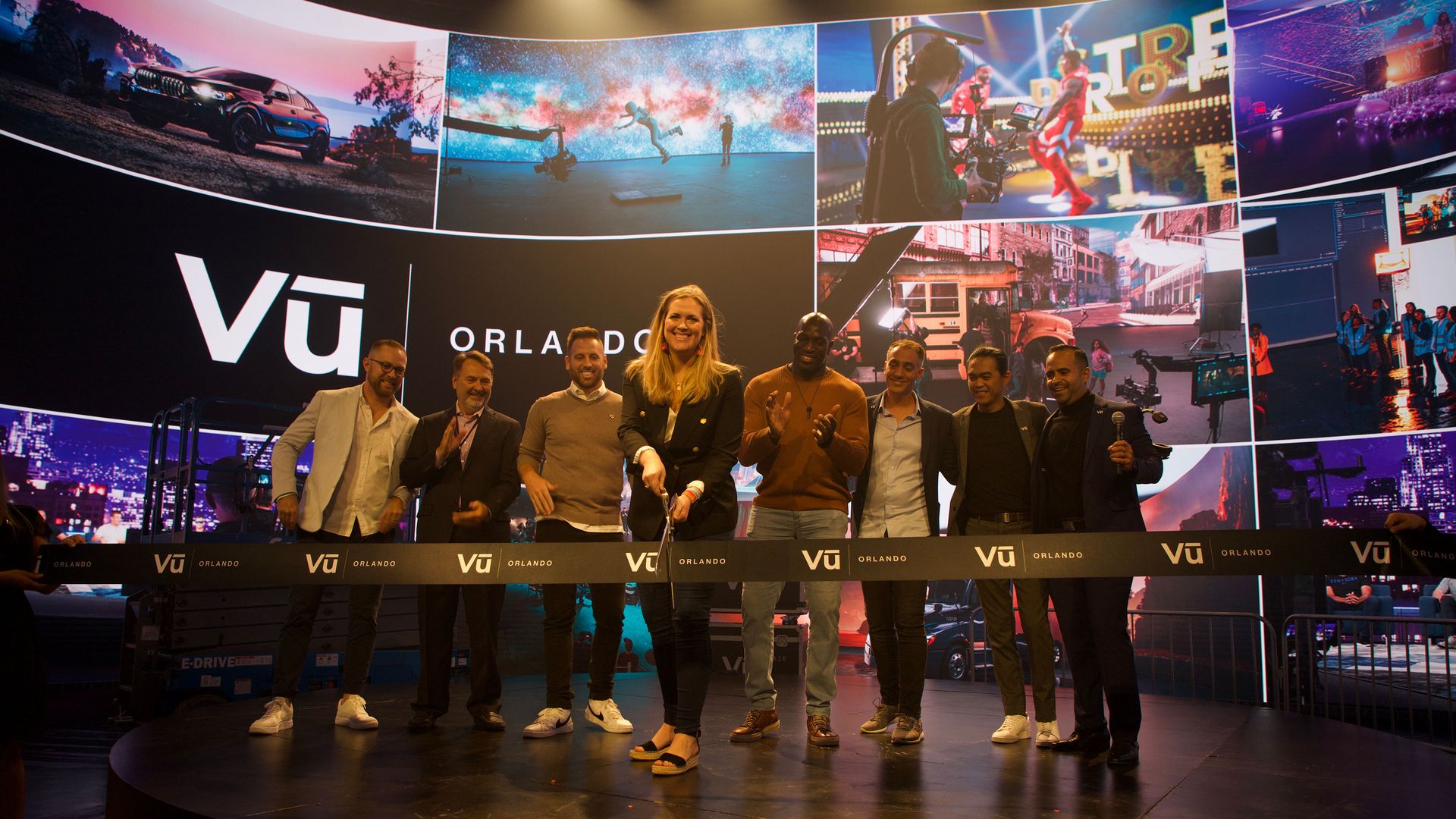 people clapping as a woman cuts a ribbon in front of the Vū screen
