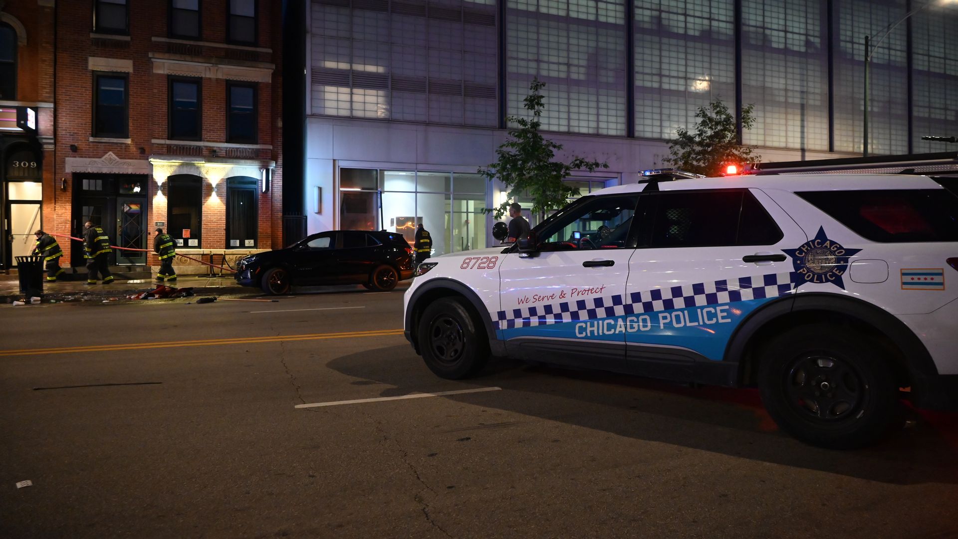 Photo of a police car blocking streets while fireman clean up sidewalk. 