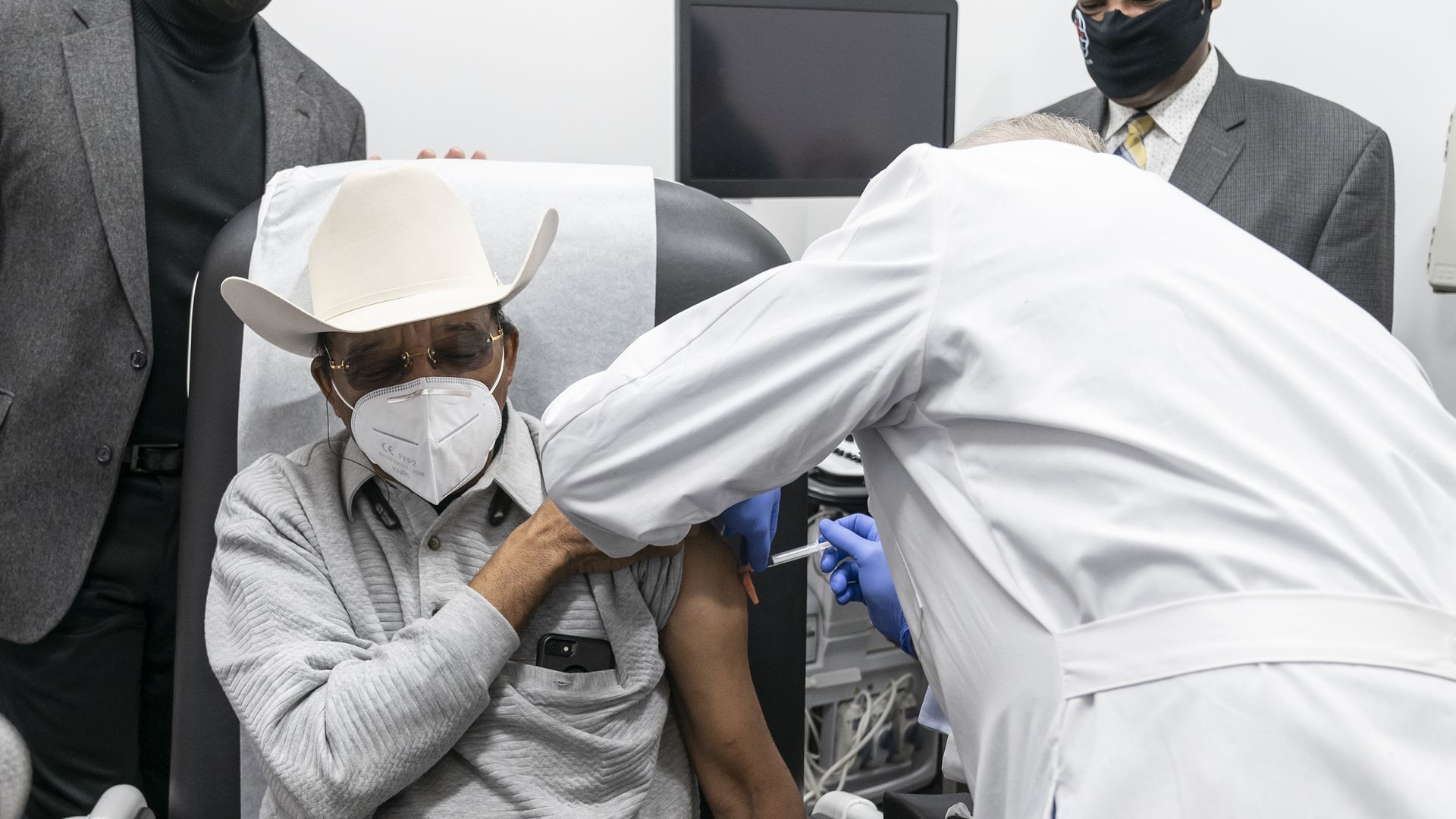 Picture of a doctor wearing a white coat administering a vaccine to a person wearing a cowboy hat