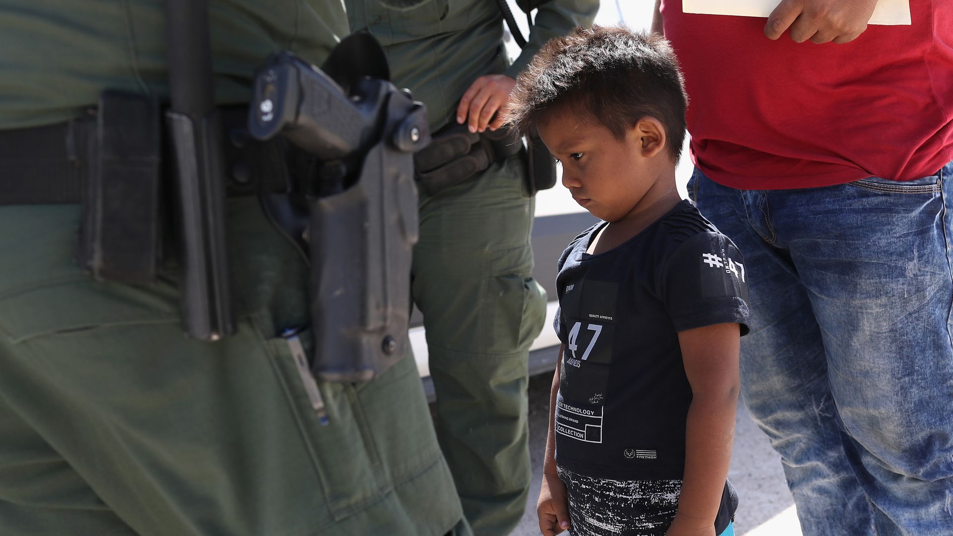 A migrant child is surrounded by border patrol officers