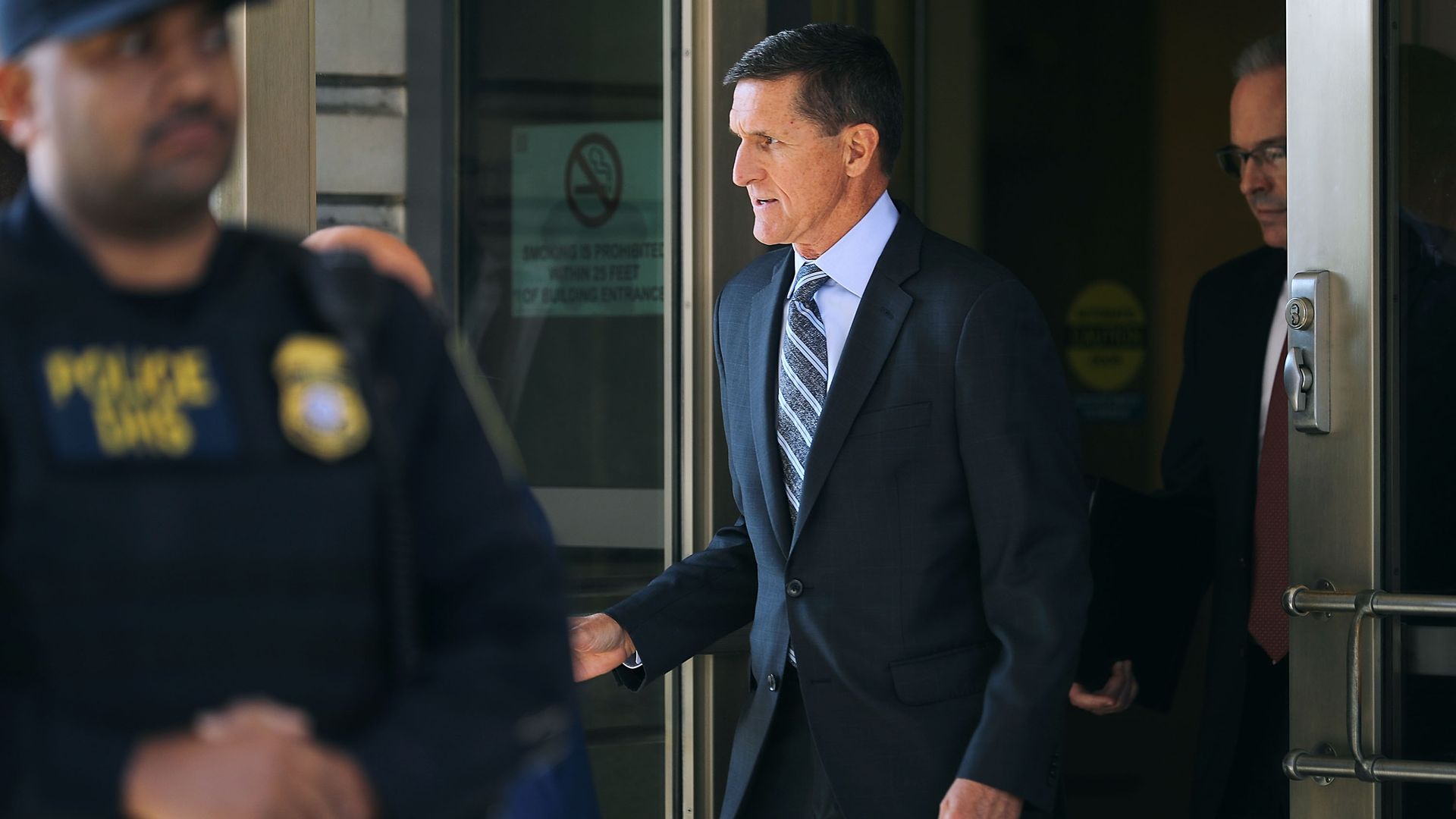 Michael Flynn wears a suit and walks out of a door.