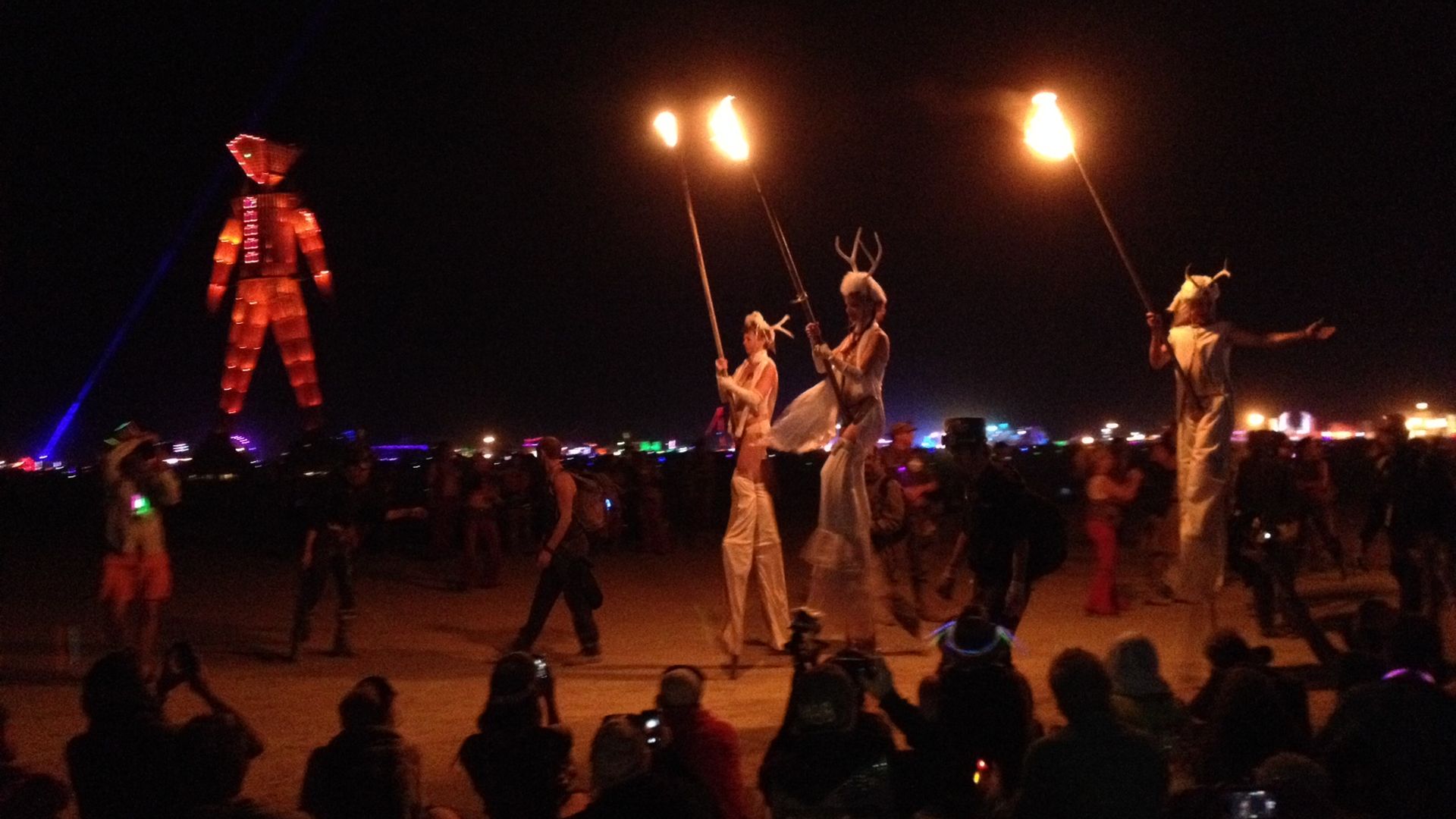 A parade of torch-bearers approaches an effigy of a man that's about to be set on fire at the Burning Man festival.
