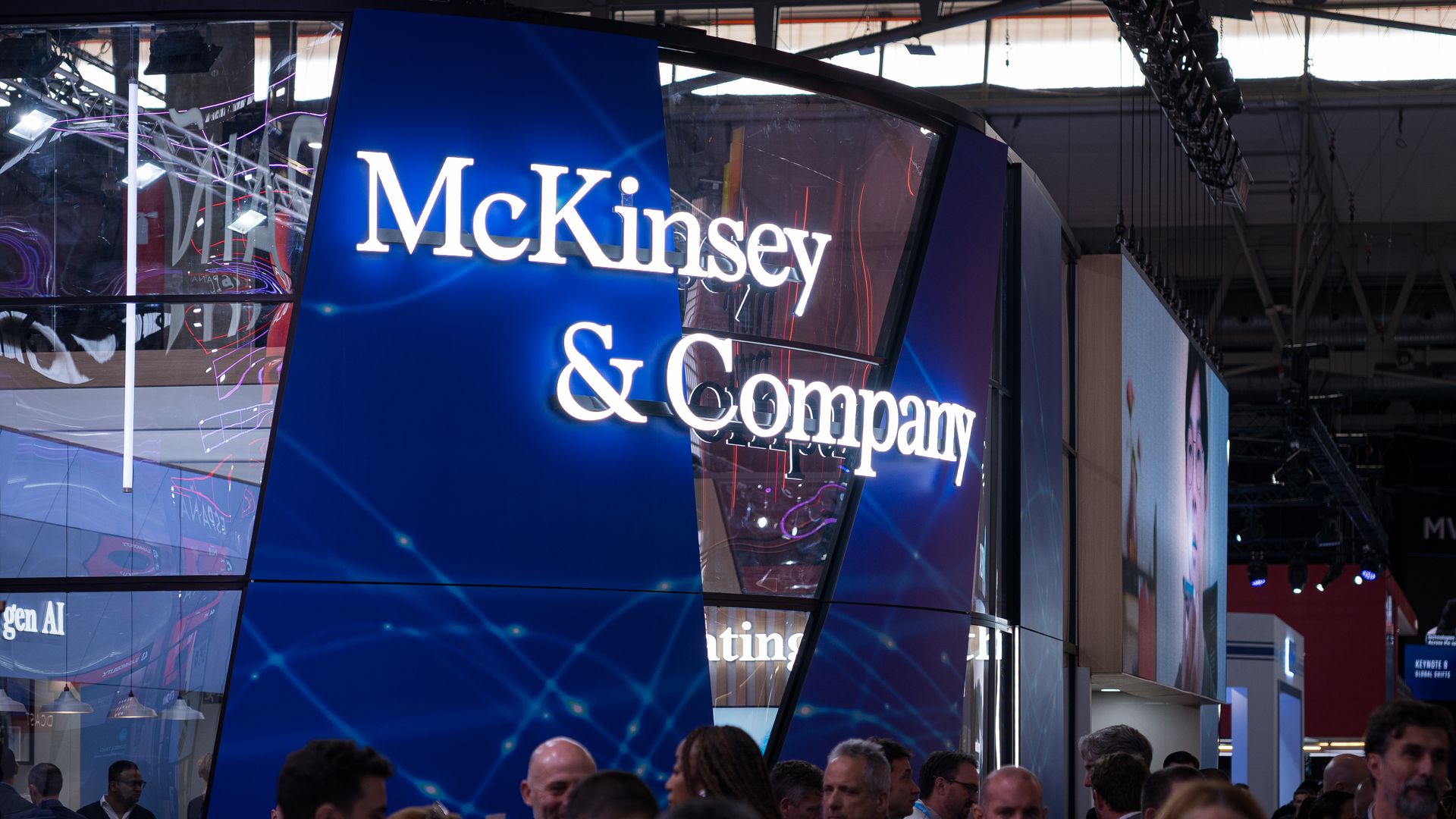 Crowd of people gathered near a large blue McKinsey & Company booth with bright white illuminated signage at an indoor event or conference.
