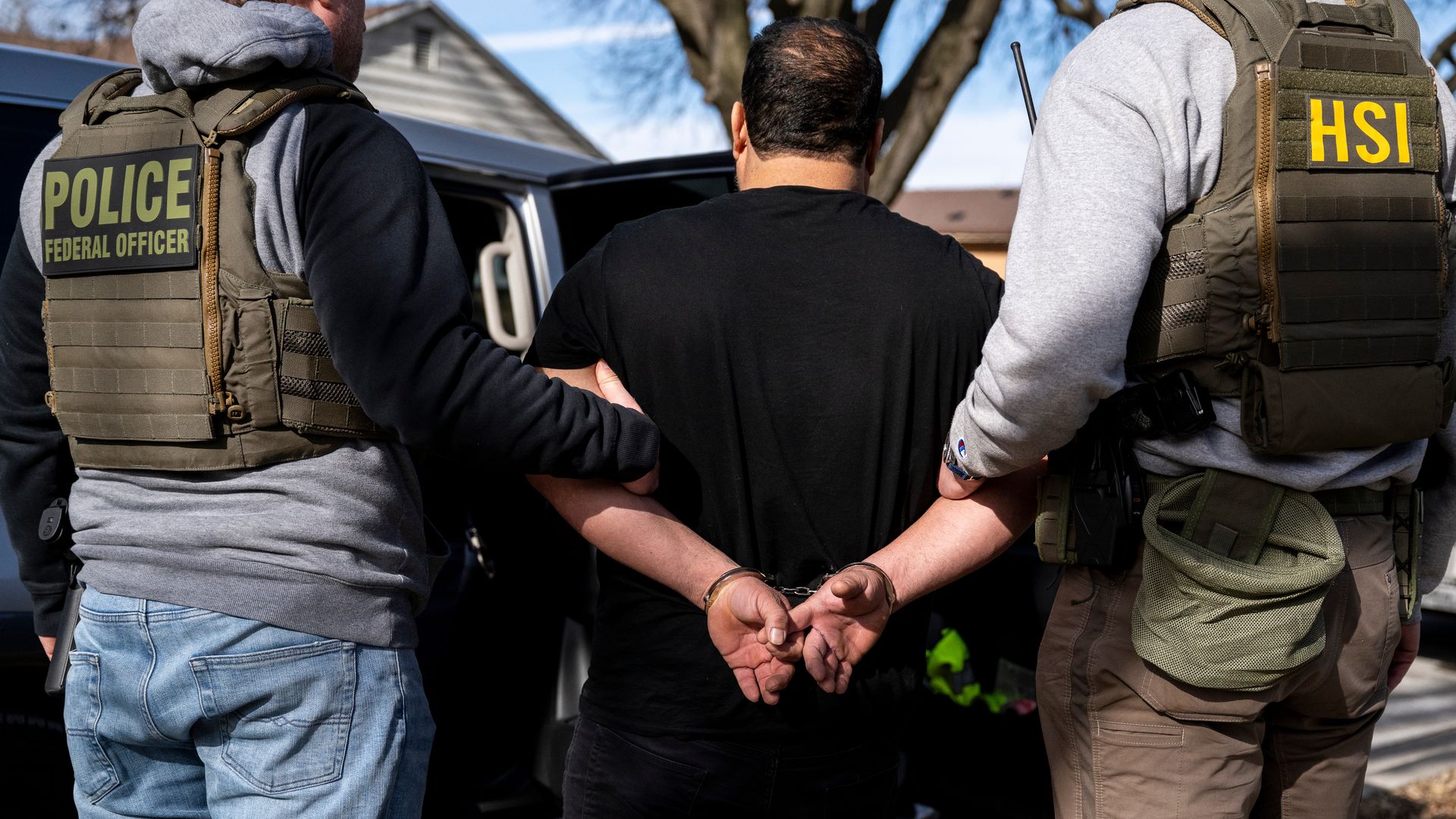 Two law enforcement officers hold onto a detainee arrested during an immigration raid.