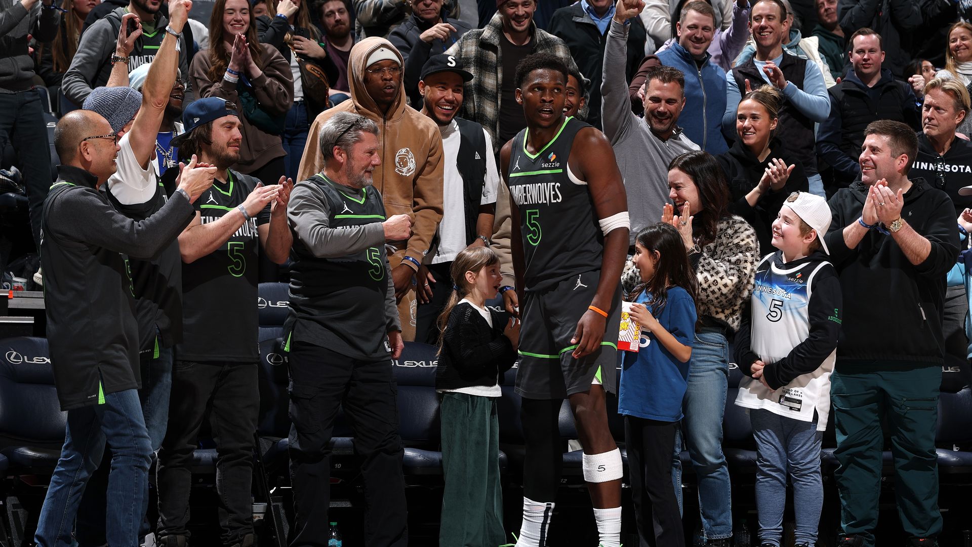 Fans in Wolves gear cheer for Anthony Edwards as he stands in front of them wearing a black team jerset. 