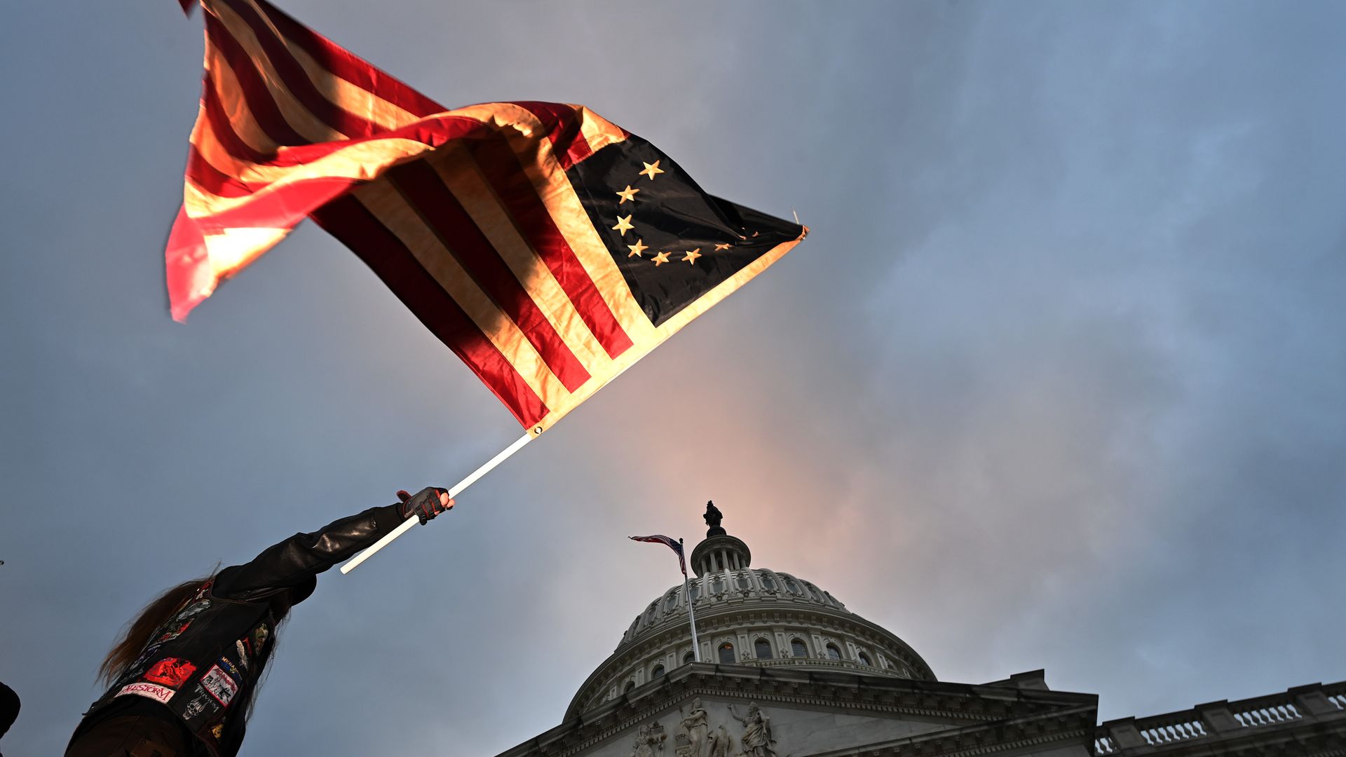 Photo of a Trump supporter waving an American flag in the sky against the Capitol building's backdrop