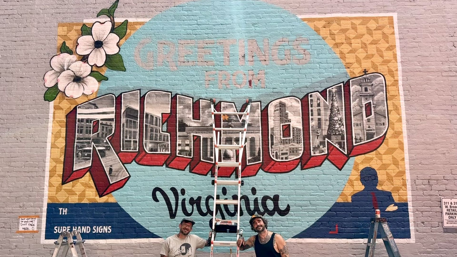Colorful mural on a brick wall with a turquoise circle, the words "Greetings from Richmond, Virginia" in photo-filled letters, white hibiscus on the left, ladders in front, and two men posing at the bottom.