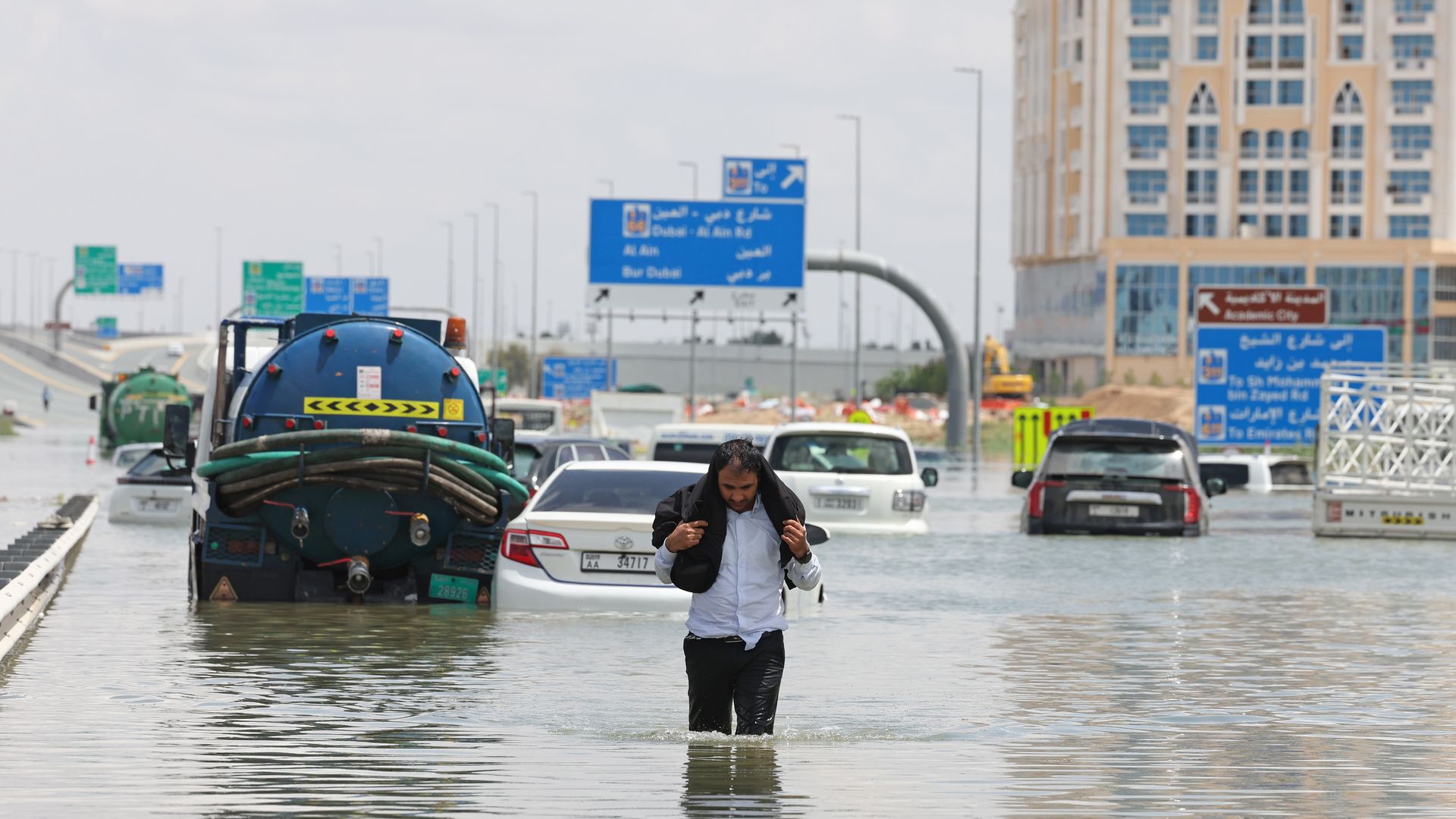 A man holding his jacket walks through a flooded highway in Dubai.