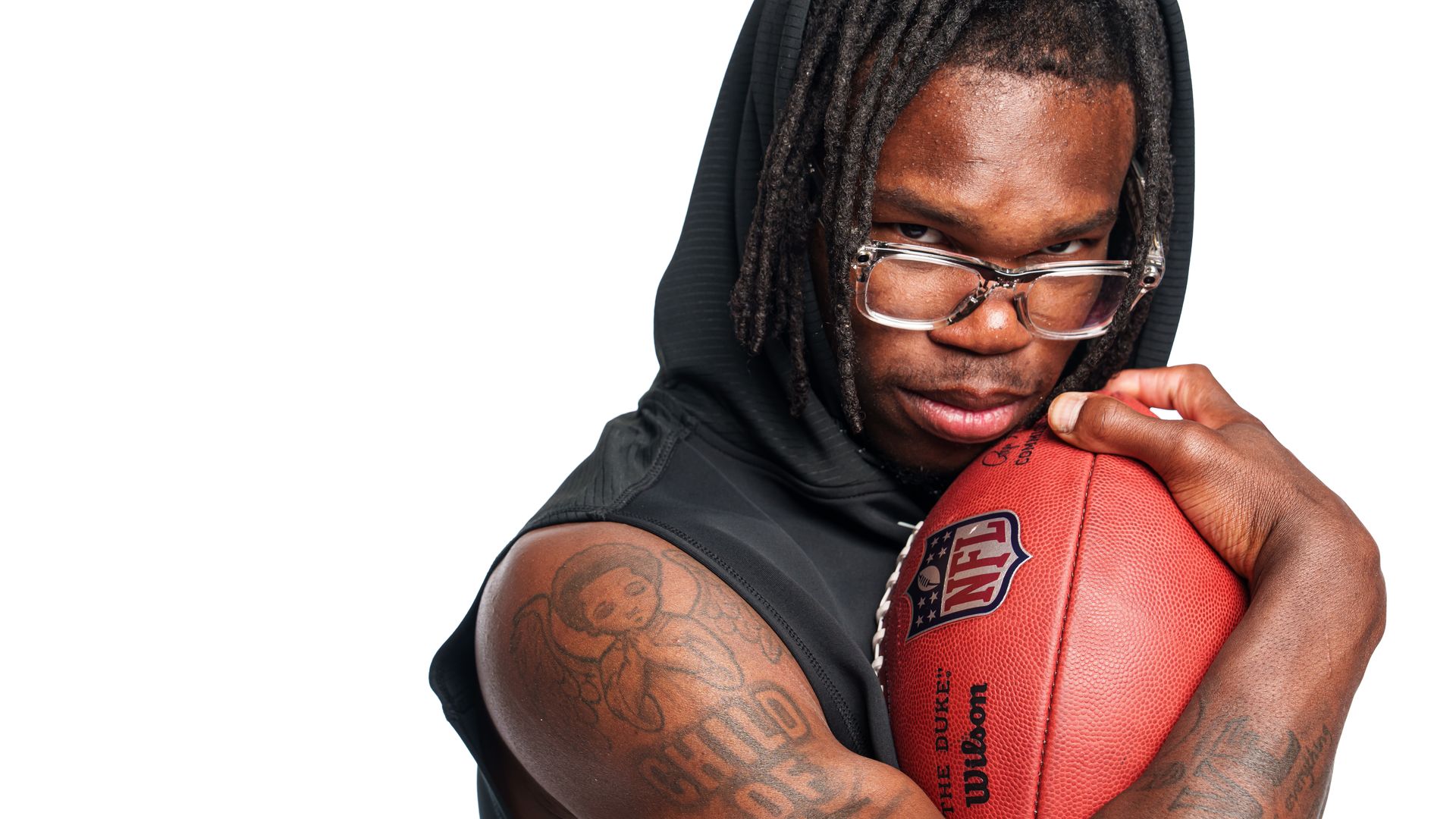 Football player Travis Hunter poses with a football agains this flexed bicep. 