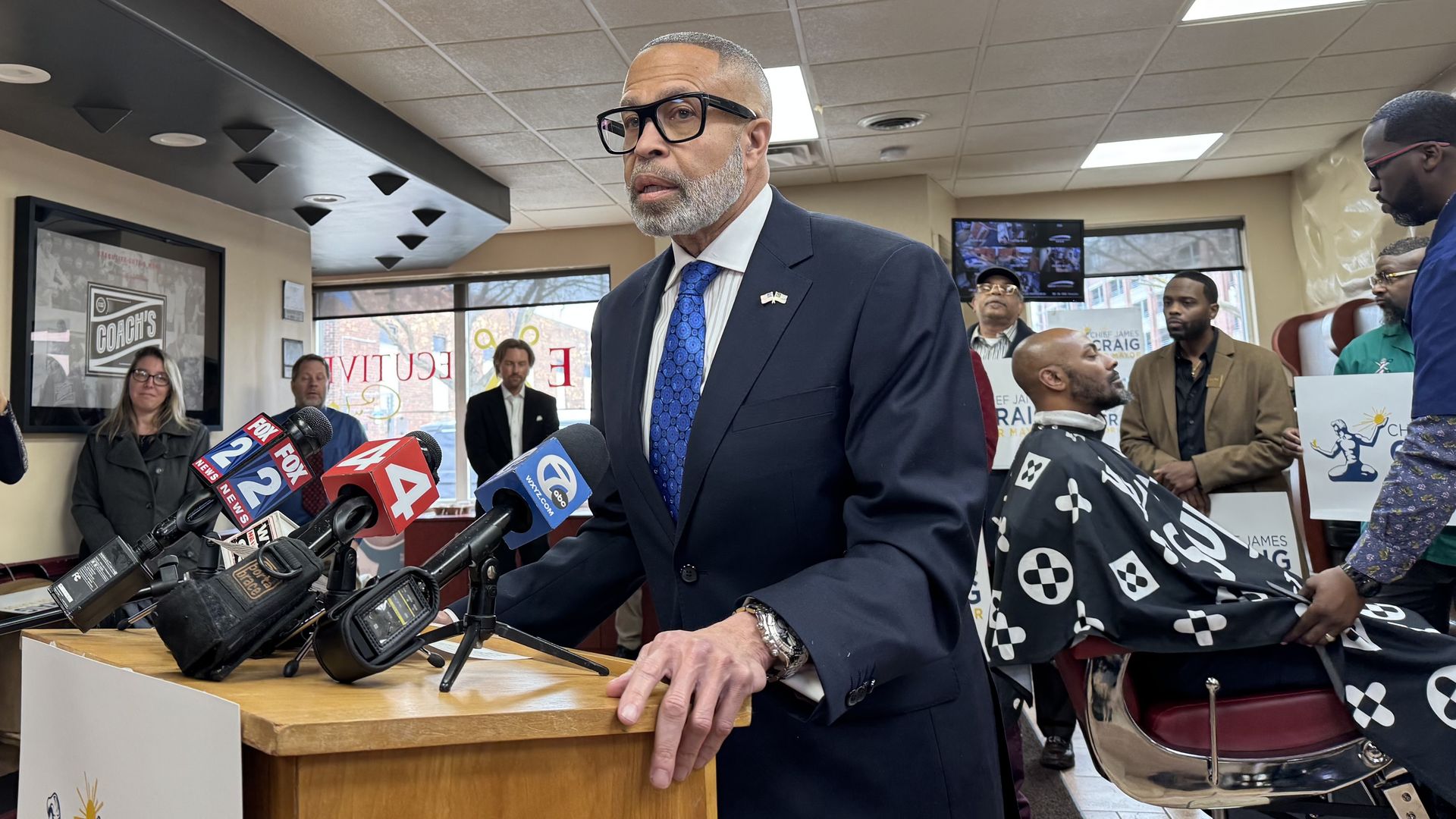 James Craig stands at a podium in a barber's shop
