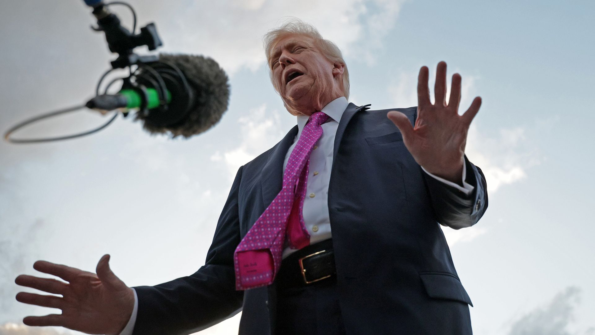 President Trump, seen from a low angle looking up, gestures while speaking to a microphone. 