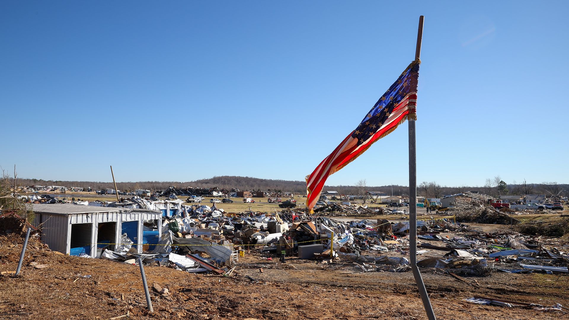 An american flag standing in front of rubble left behind from a tornado.