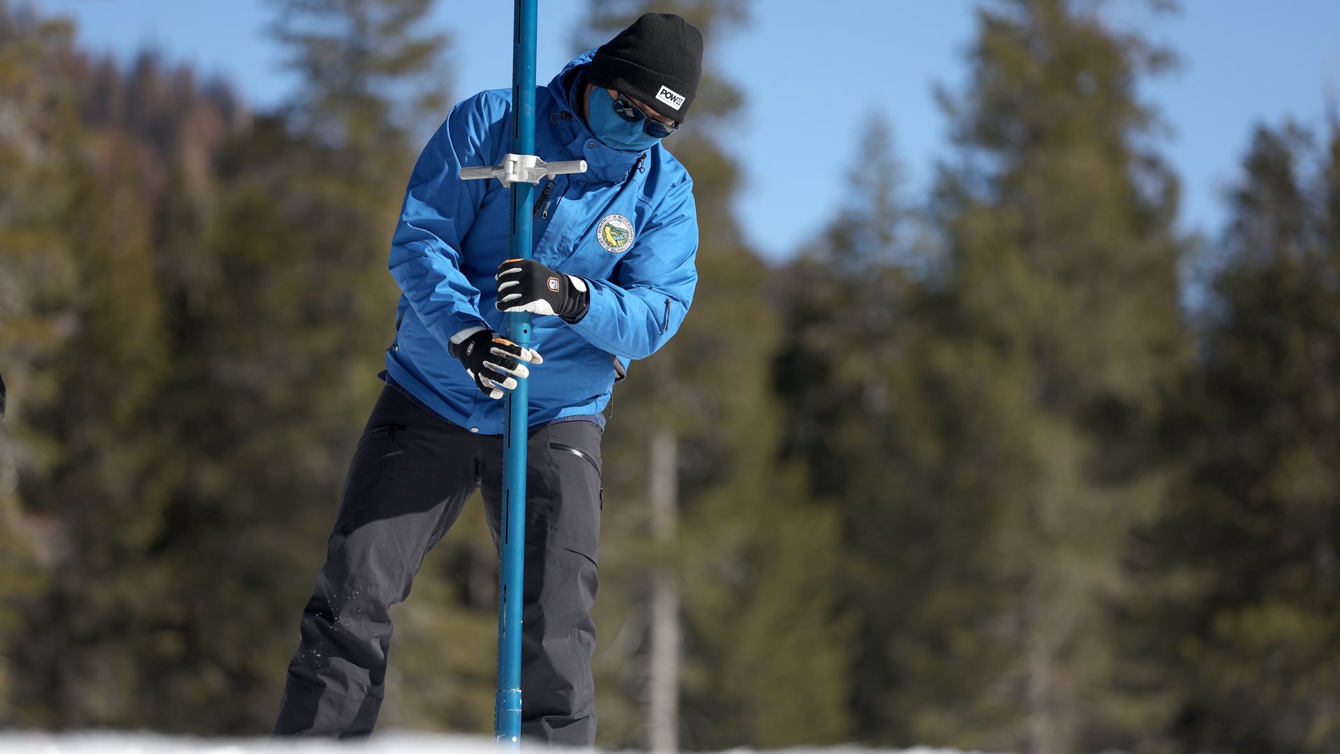 Man driving a measuring stick into snow cover to determine its depth.
