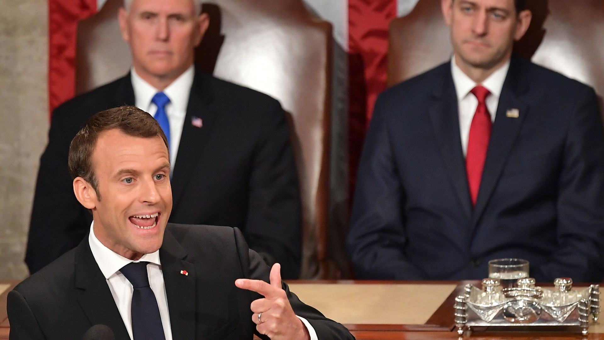 Emmanuel Macron gestures while speaking, with Mike Pence and Paul Ryan sitting behind him.