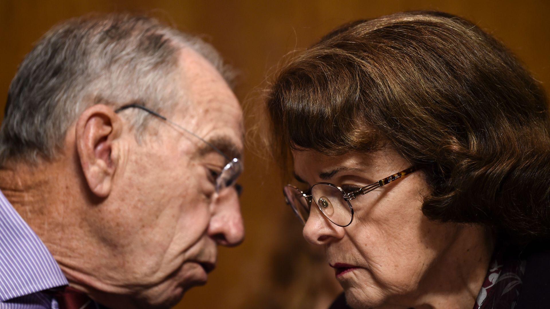 Feinstein and Grassley huddle and talk with bent heads.