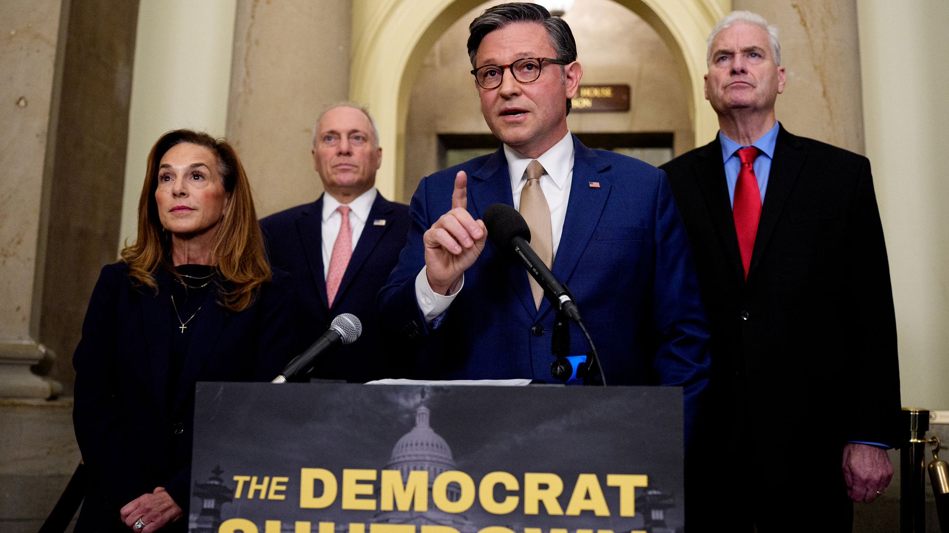 Speaker Johnson at a press conference with Reps. McClain, Emmer and Scalise behind him. A sign below him reads "the Democrat shutdown"
