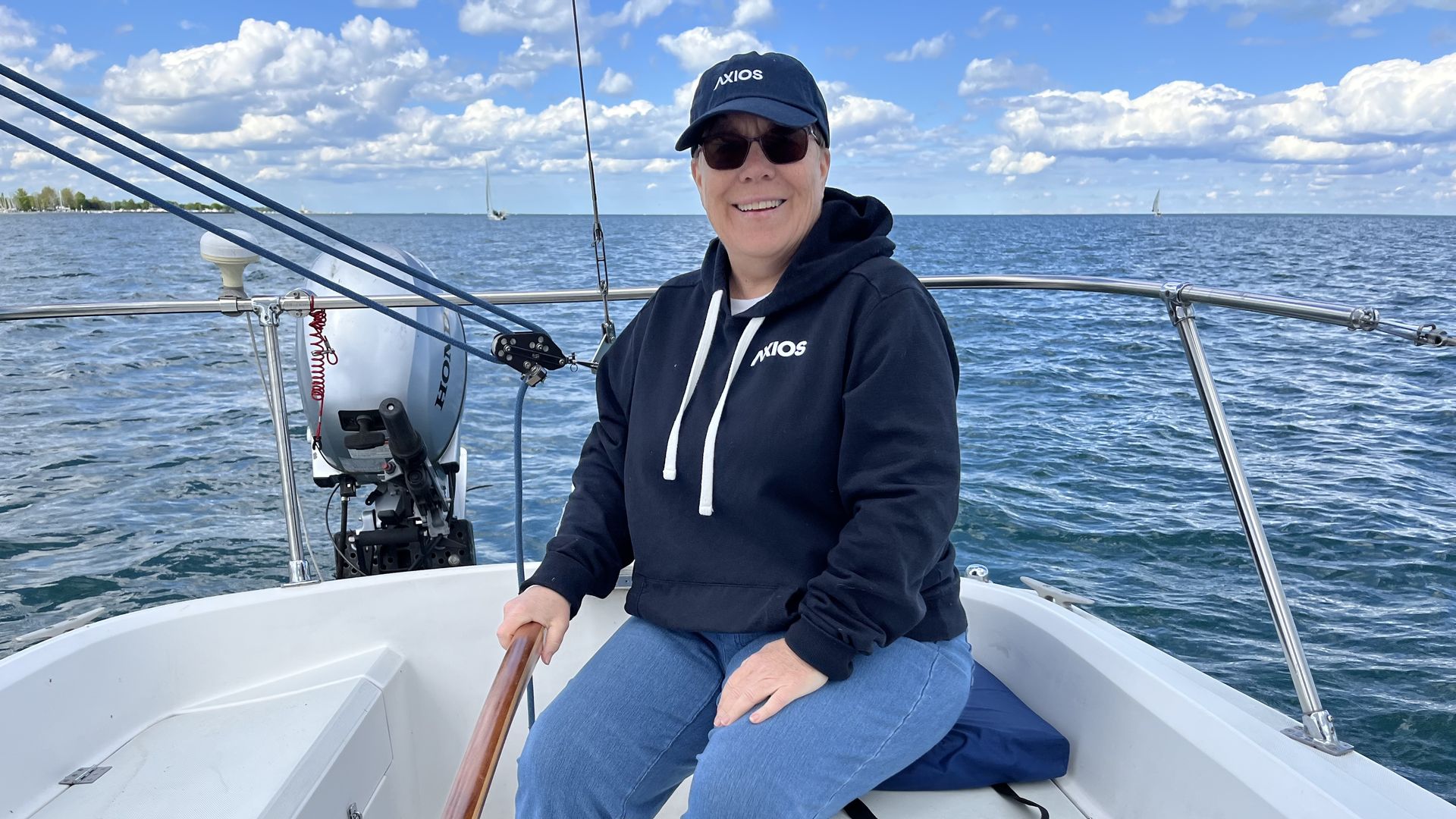 Image of the author in a hoodie sweatshirt and cap, sailing her sailboat in Lake Saint Clair near Detroit. 