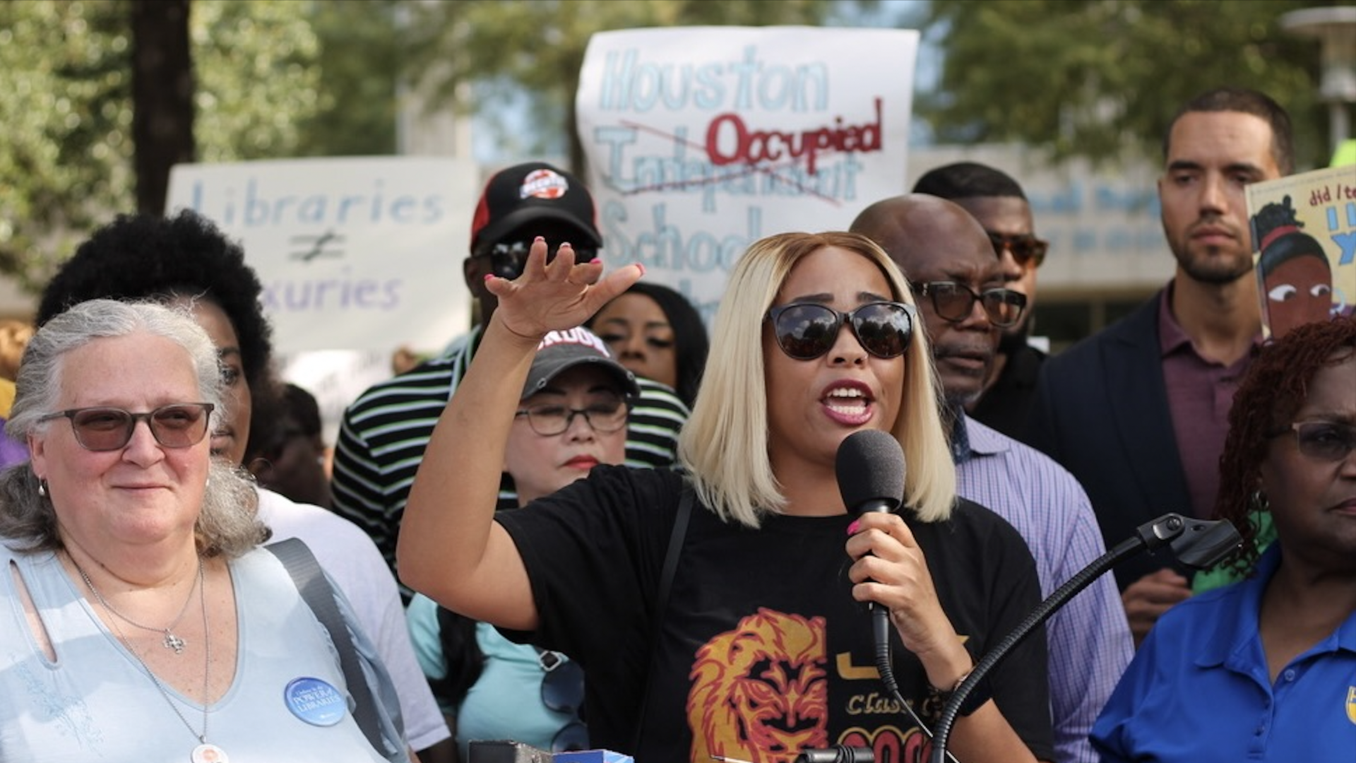 Photo of a woman at a rally with a crowd behind her.