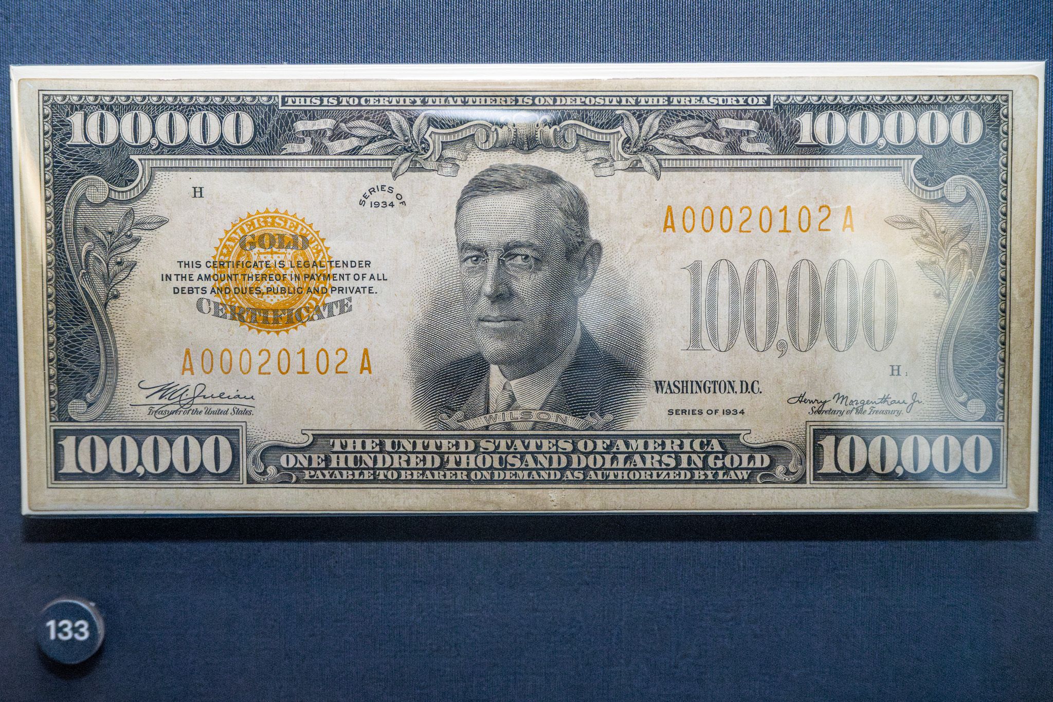 Close-up of a 1934 United States Gold Certificate worth $100,000, with a portrait of Woodrow Wilson in the center, ornate blue border, large "100,000" numerals in the corners, and a gold seal.