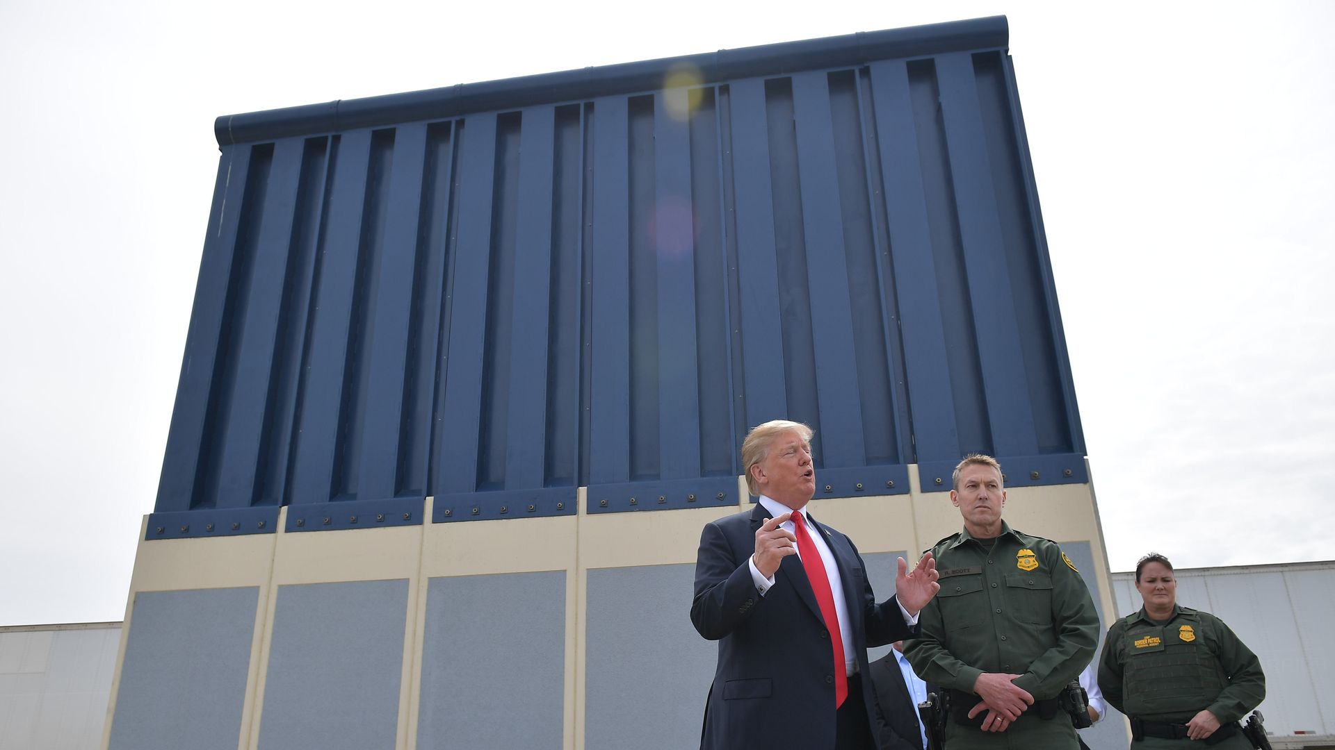 In this image, Trump talks while standing next to two border patrol officers in front of a test segment of border wall.