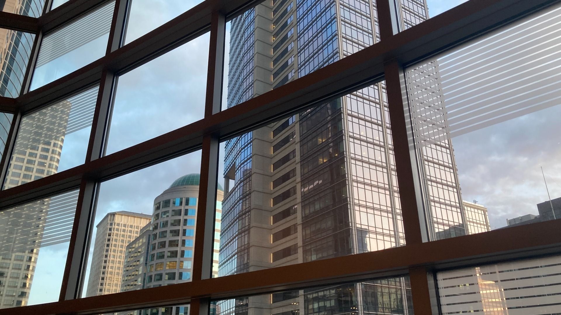 Skyscrapers loom behind a window with criscrossing black frames.