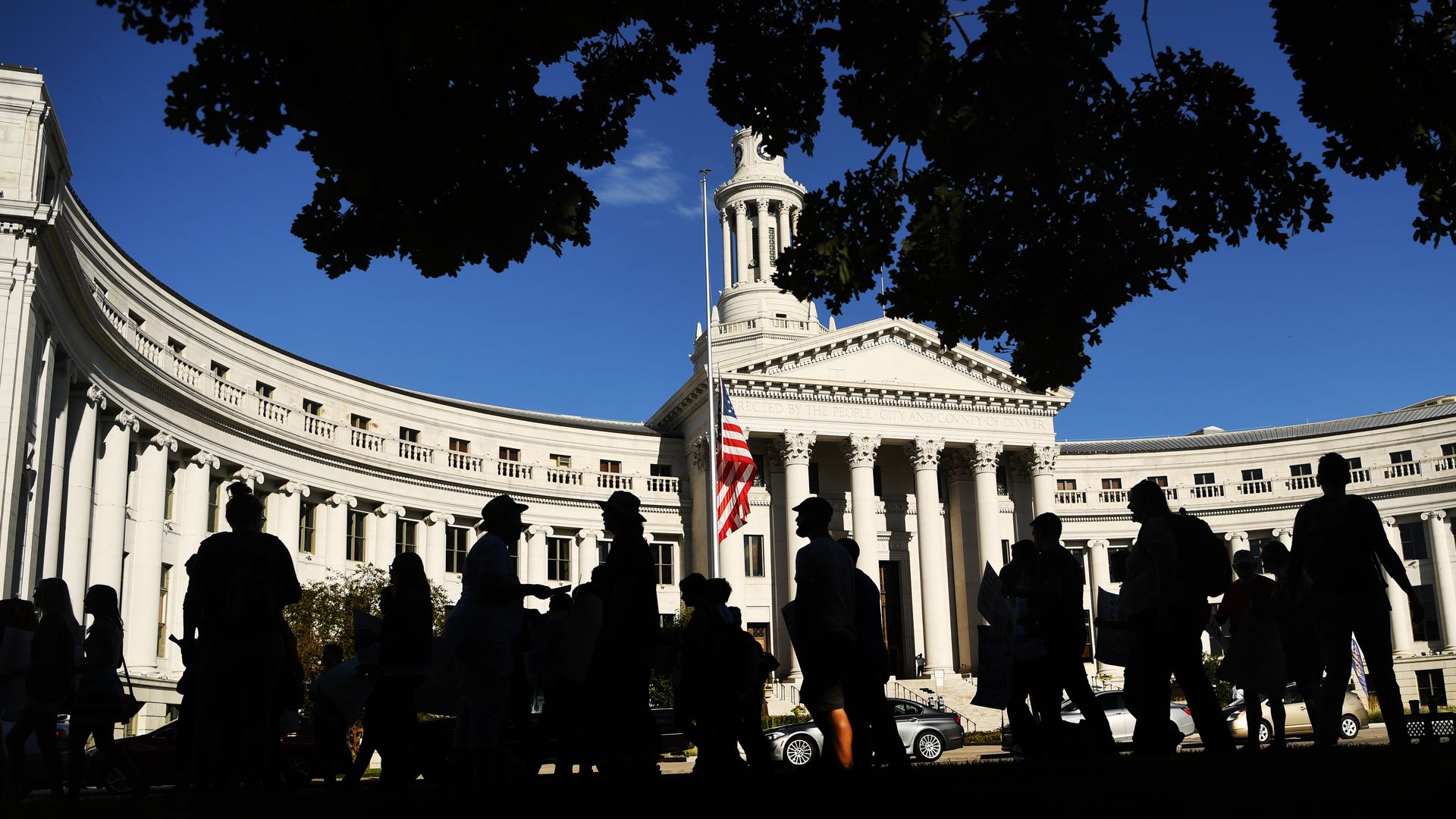 A photo of silhouettes of people outside the Denver City and County Building. 