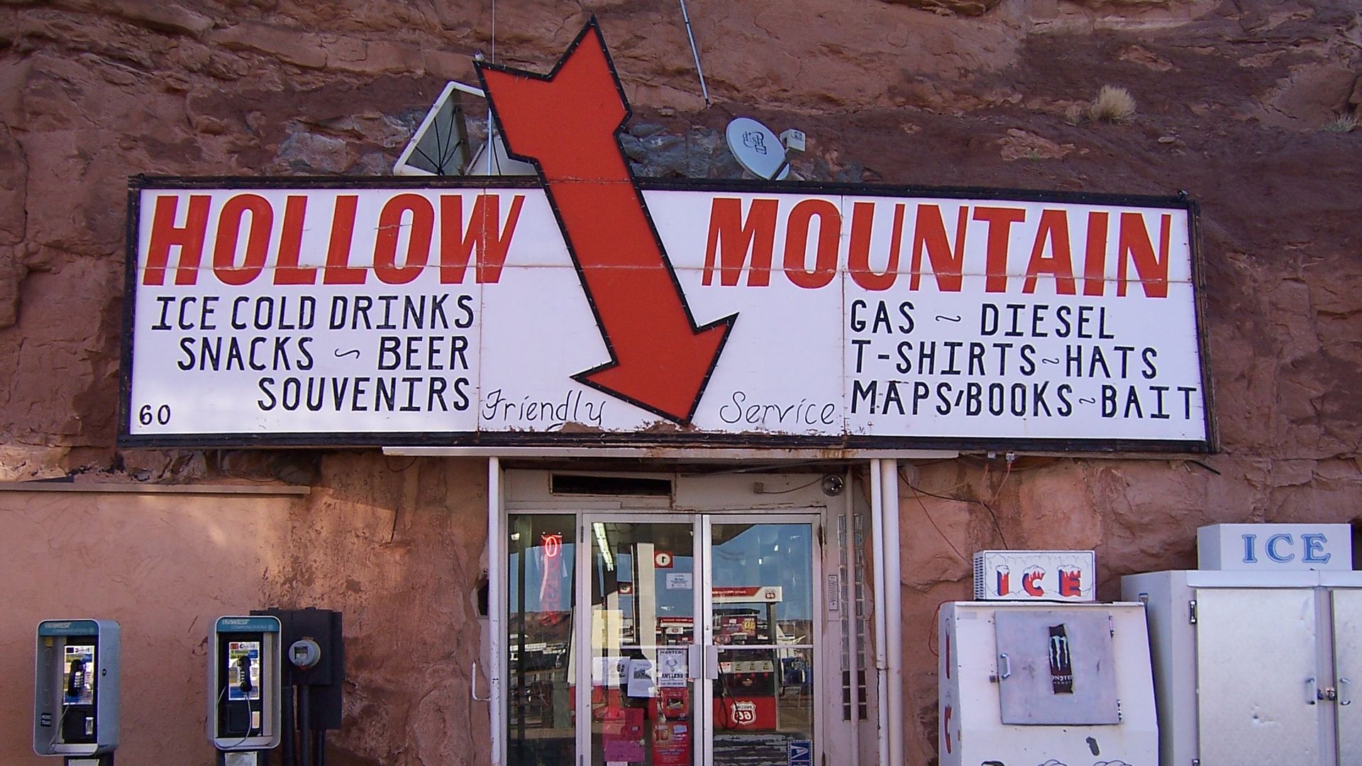 A convenience store entryway with a sign that reads "Hollow Mountain," with the store built into a red cliff.