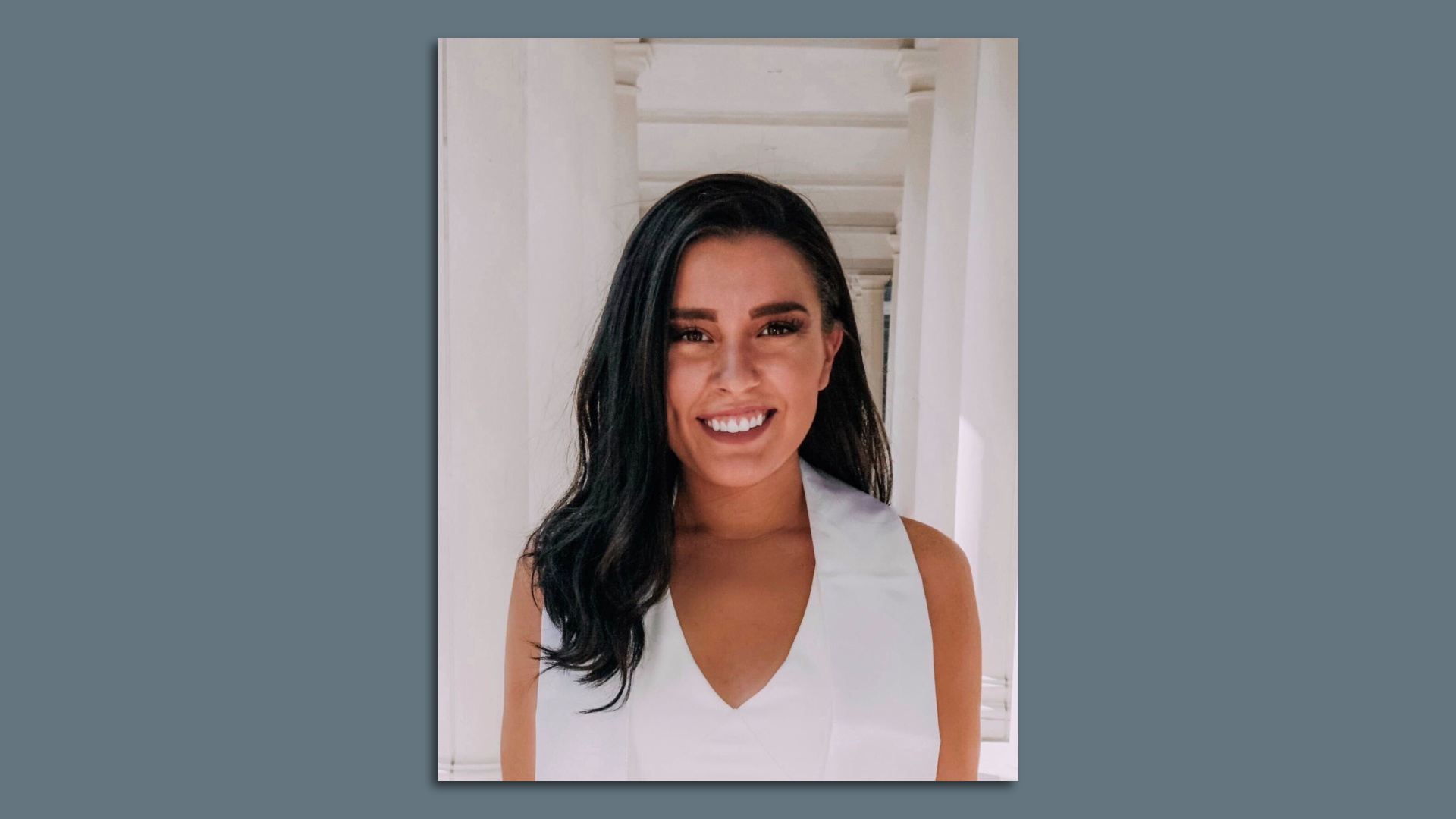 A picture of Sabrina Moreno in a white dress with her hair down smiling. The picture is bordered by a dark gray background.