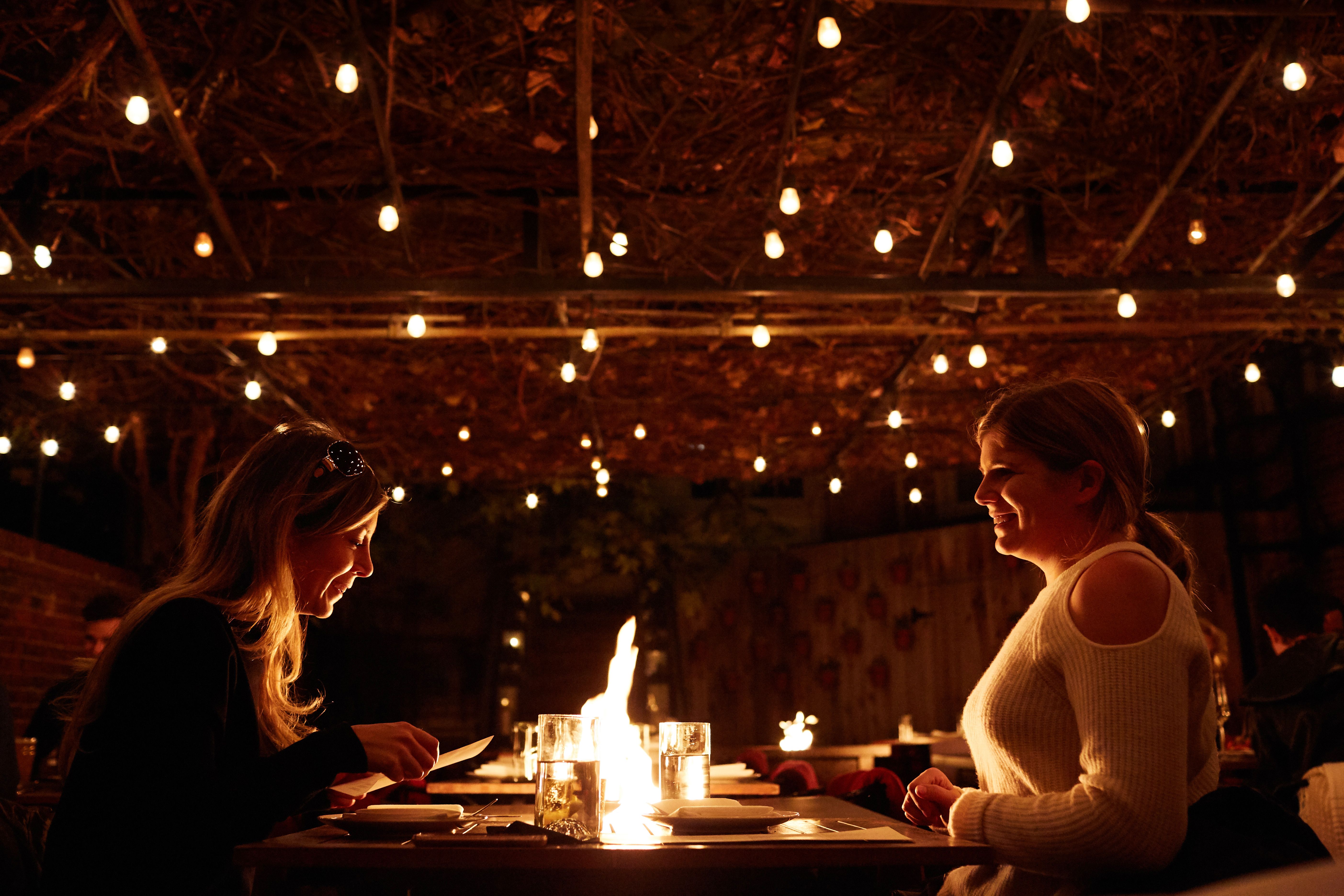 Two women sit across a fire pit table