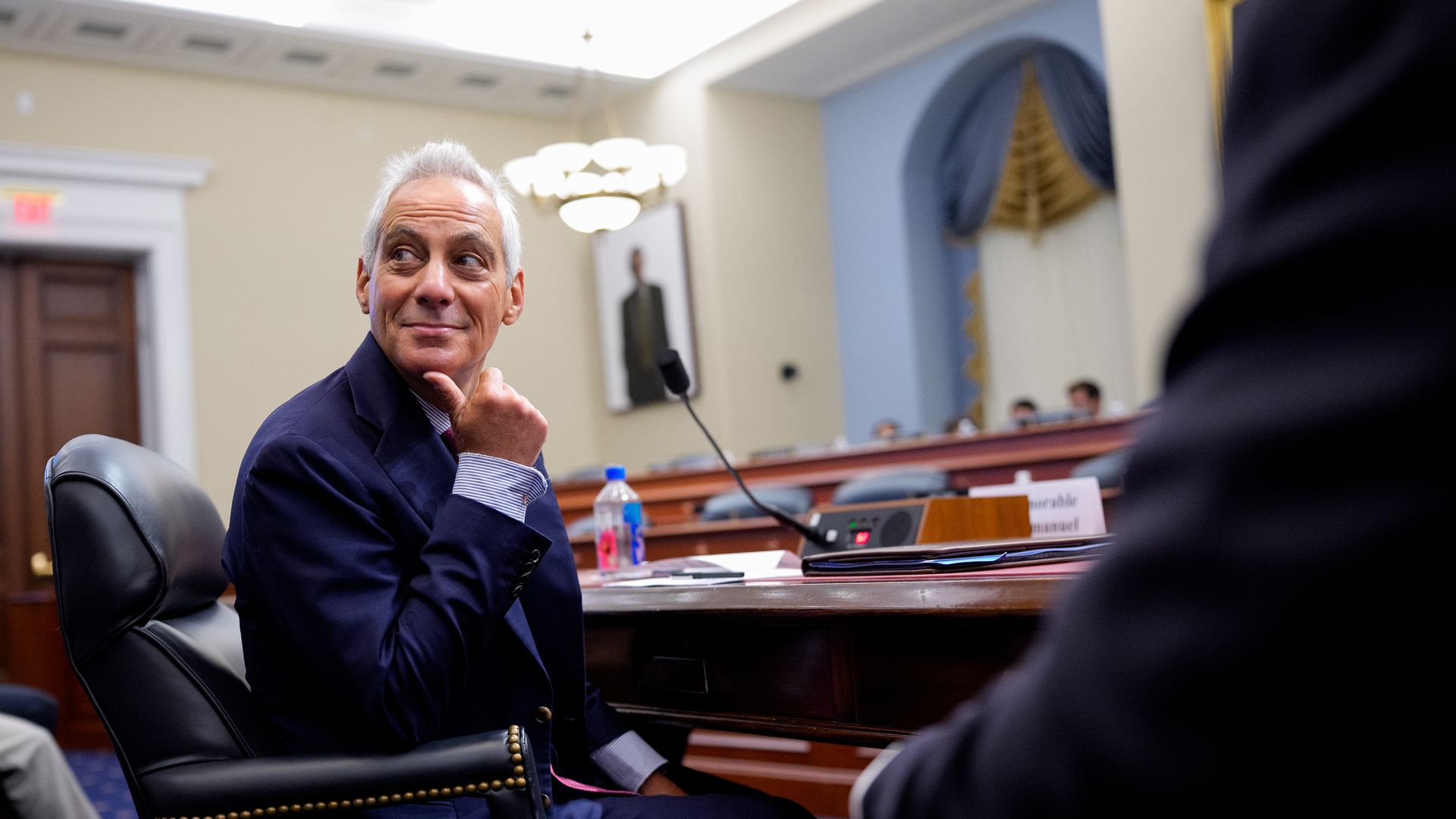 Rahm Emanuel, seated, looks to his right and smiles.