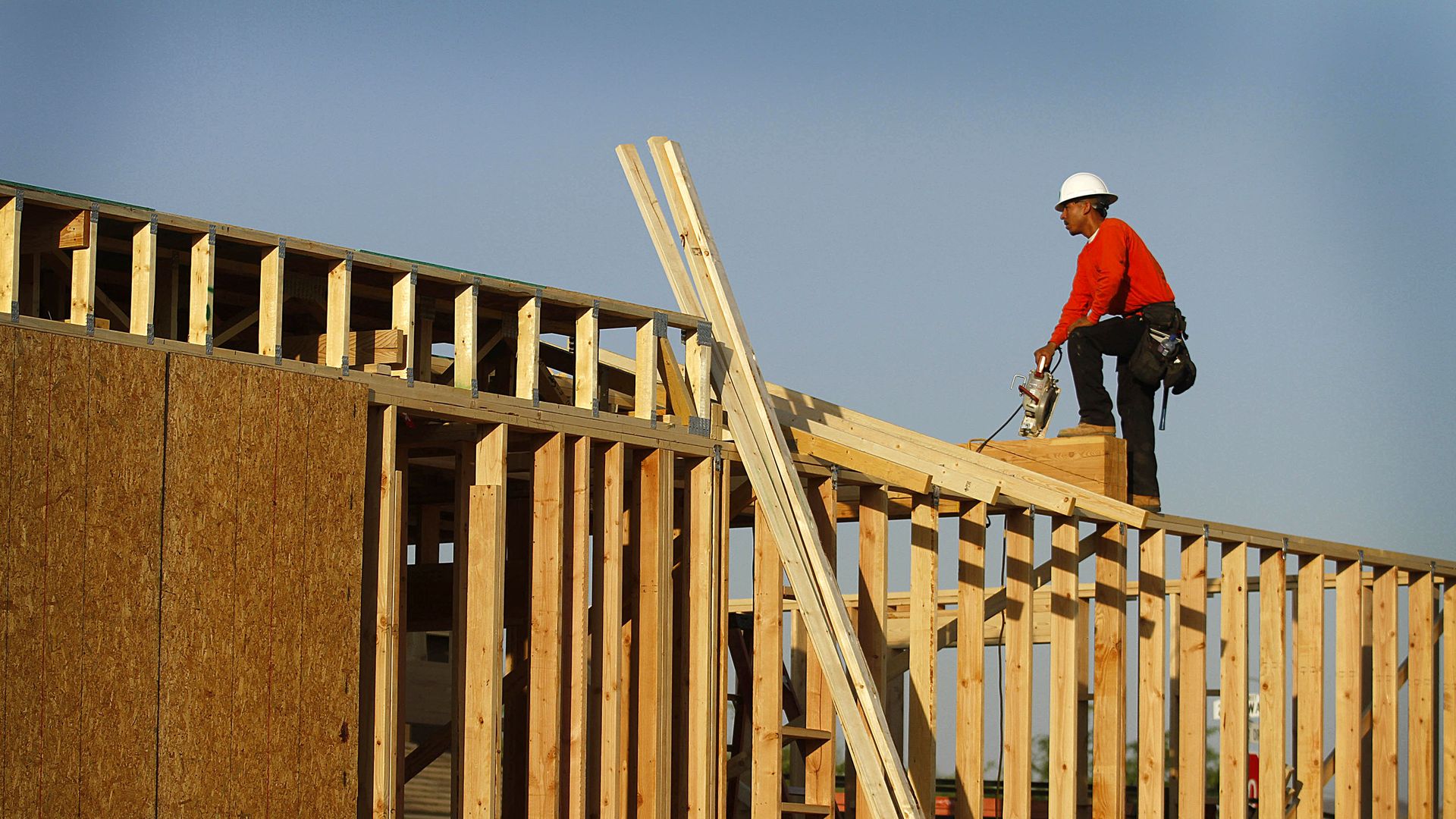 A construction worker stands atop the frame of a wall on a partially built house. 