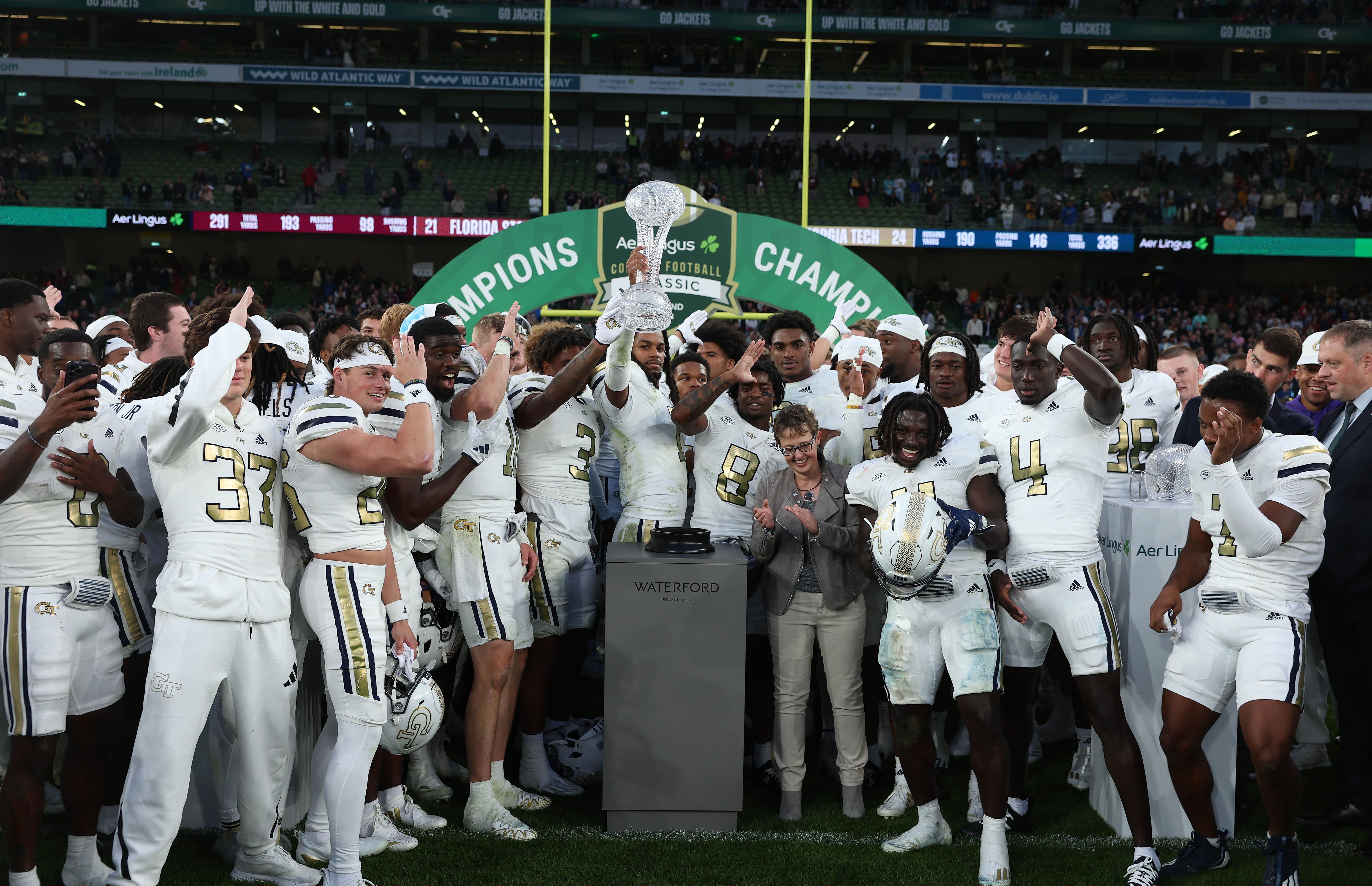 A football team in a white uniform celebrates with a trophy after winning