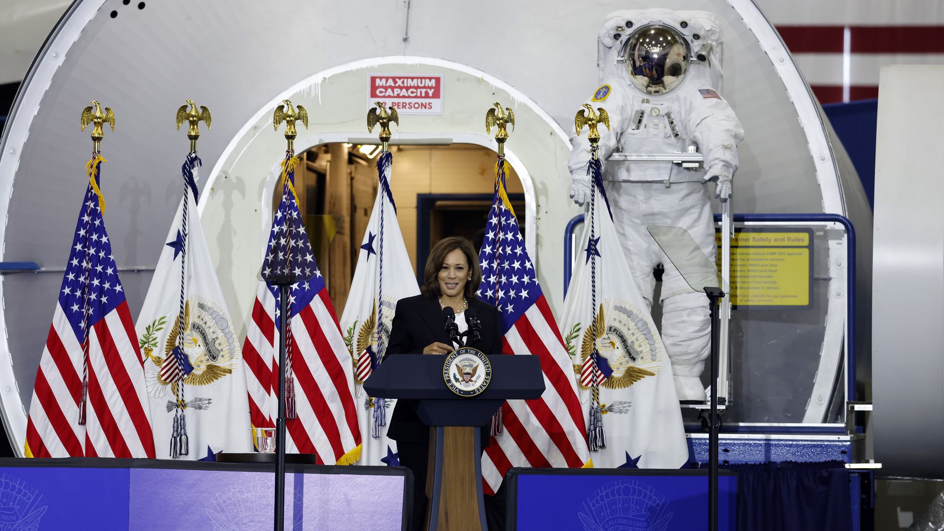 Photo of Kamala Harris in front of a large astronaut statue and American flags. 