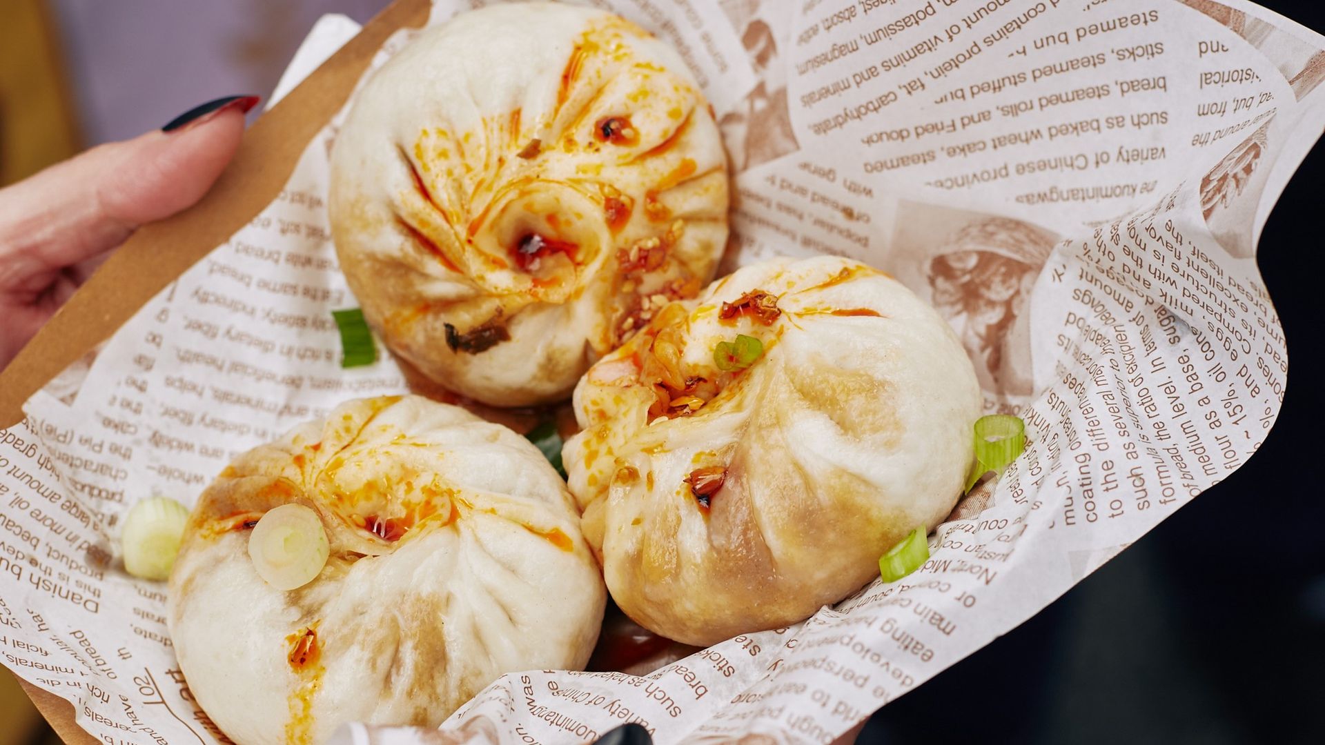 A person holding three dumplings in a bowl lined with paper.