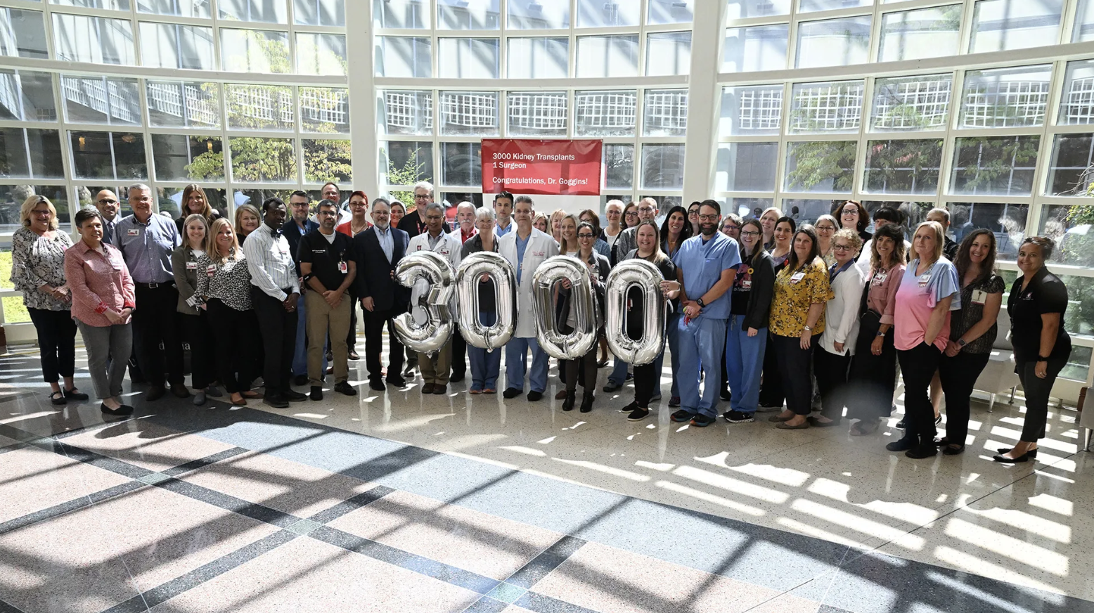Several people stand together with balloons that read "3000"