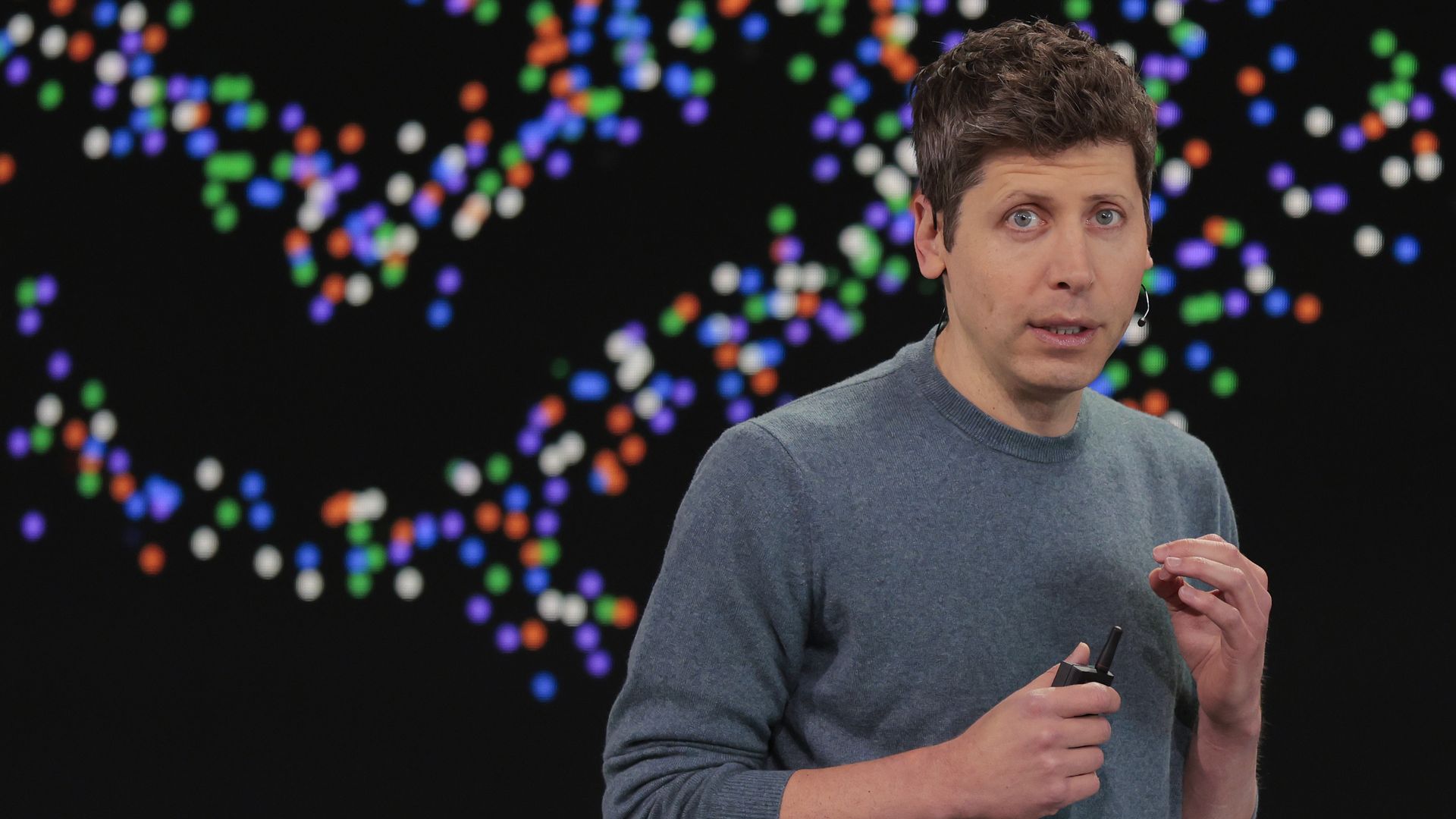 OpenAI CEO Sam Altman standing in front of a multicolored field of dots.