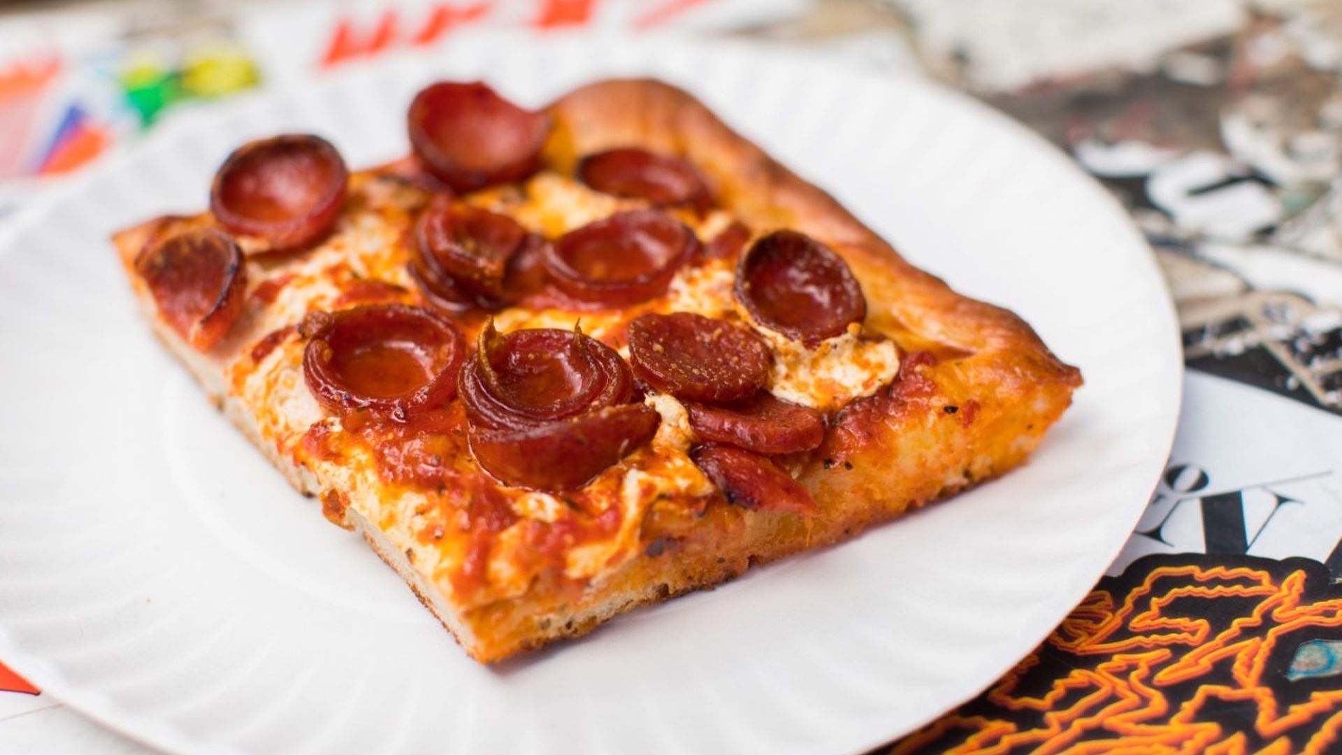 A slice of square-cut pizza on a paper plate.