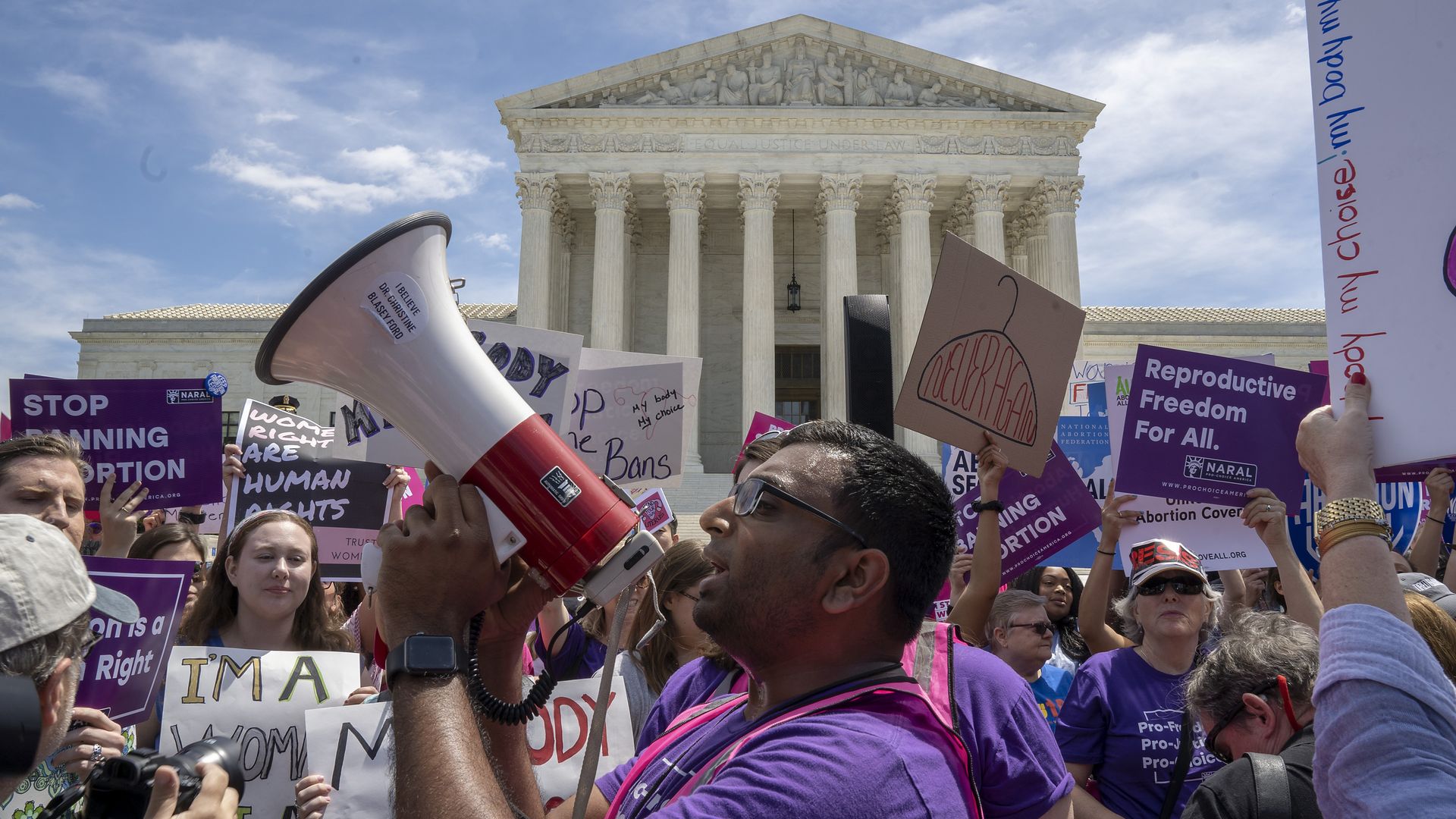 A man holds a megaphone as he leads pro-choice protester chants in front of the supreme court building.