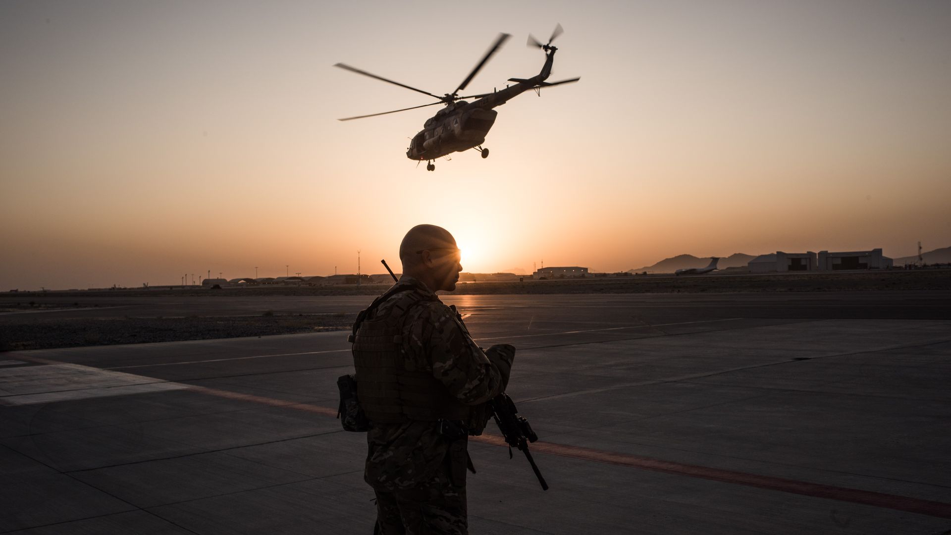 A U.S. soldier stands while a helicopter flies overhead. 