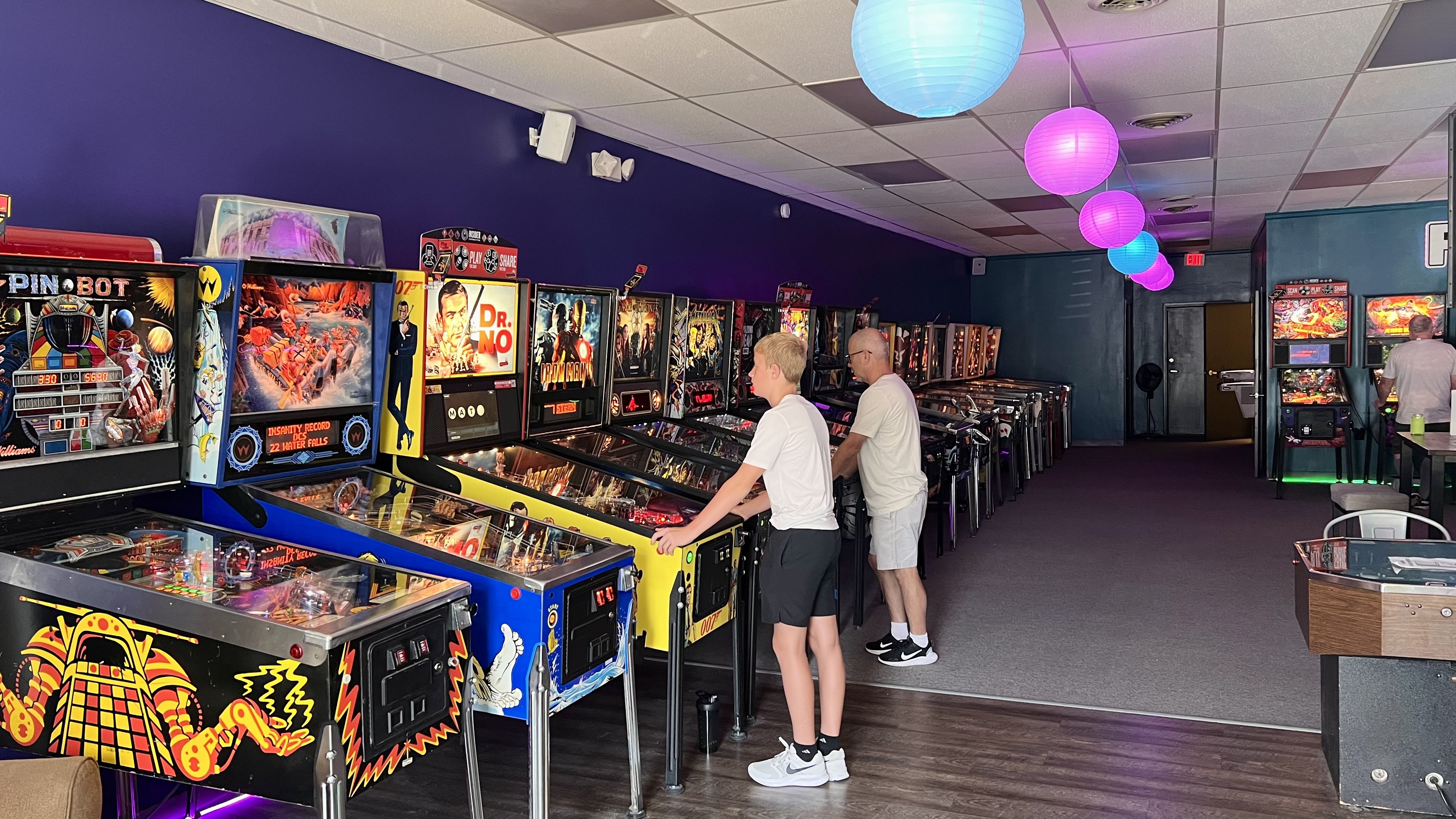 a kid and another person playing pinball machines near each other