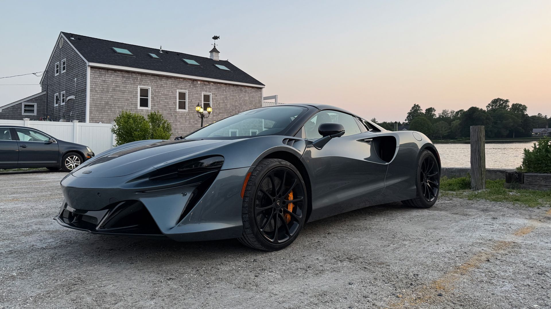 A photo of a gray McLaren Artura plug-in hybrid, parked in a waterfront parking lot.