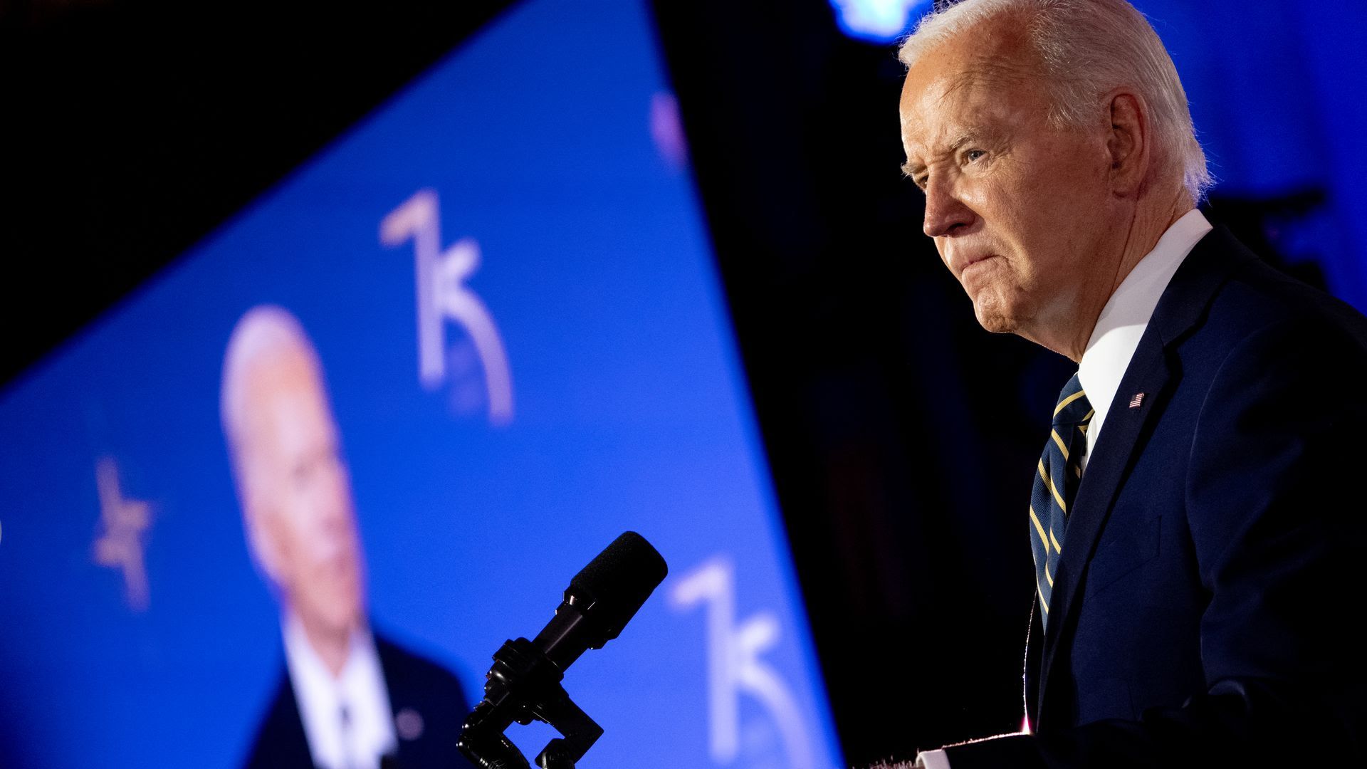 A photo of Joe Biden with a TV displaying his image in the background.