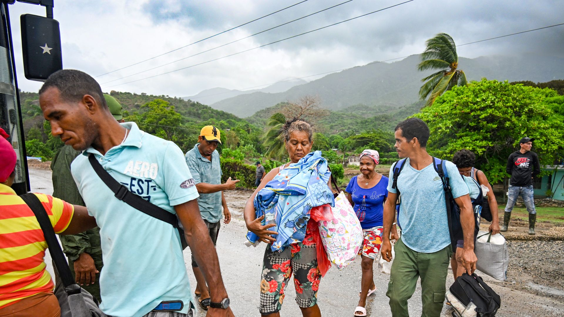 A group of people board a bus in Cuba, carrying bags and other goods as they evacuate before a storm.