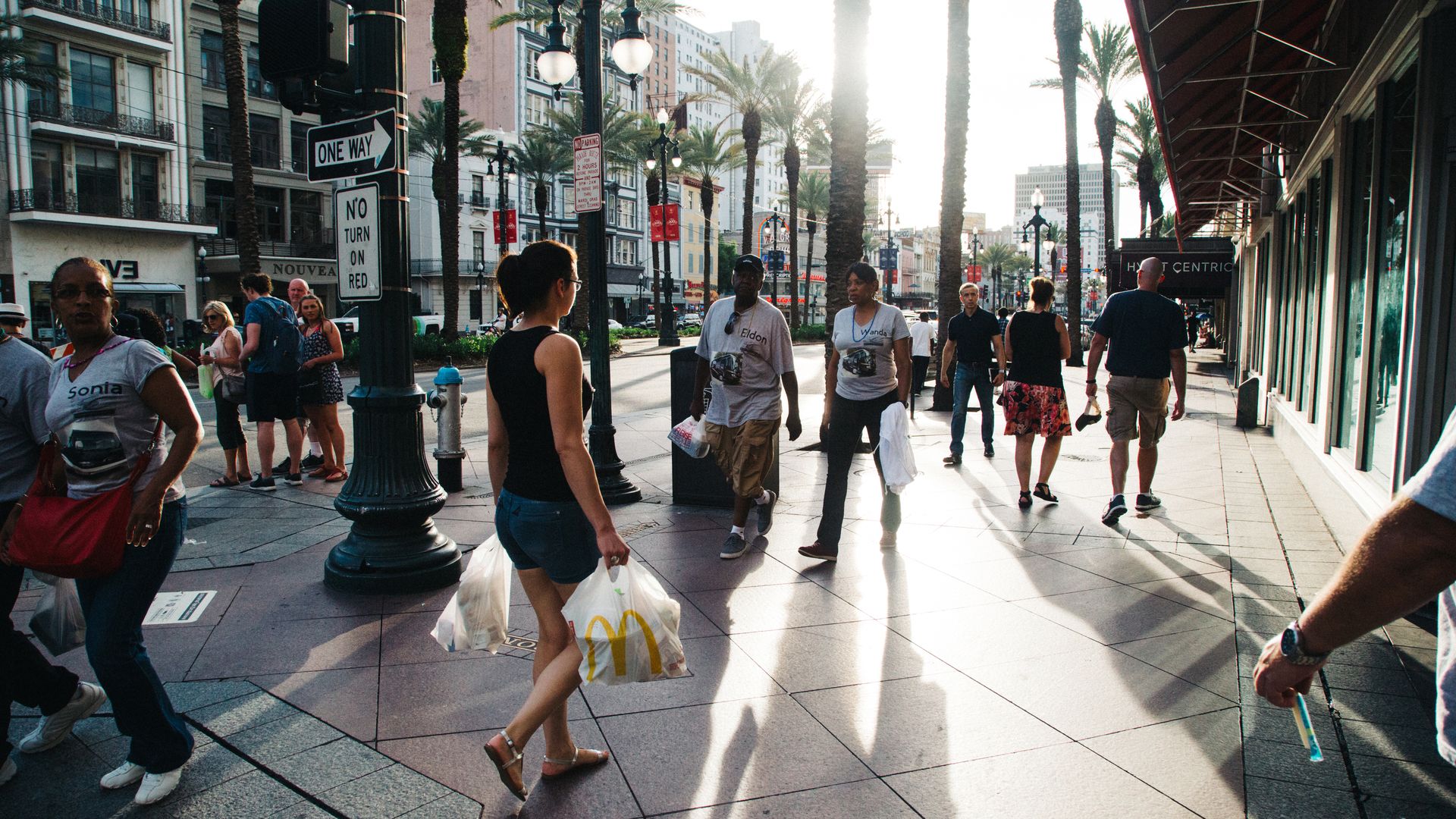 Shoppers and visitors walk along Canal Street at sunset.