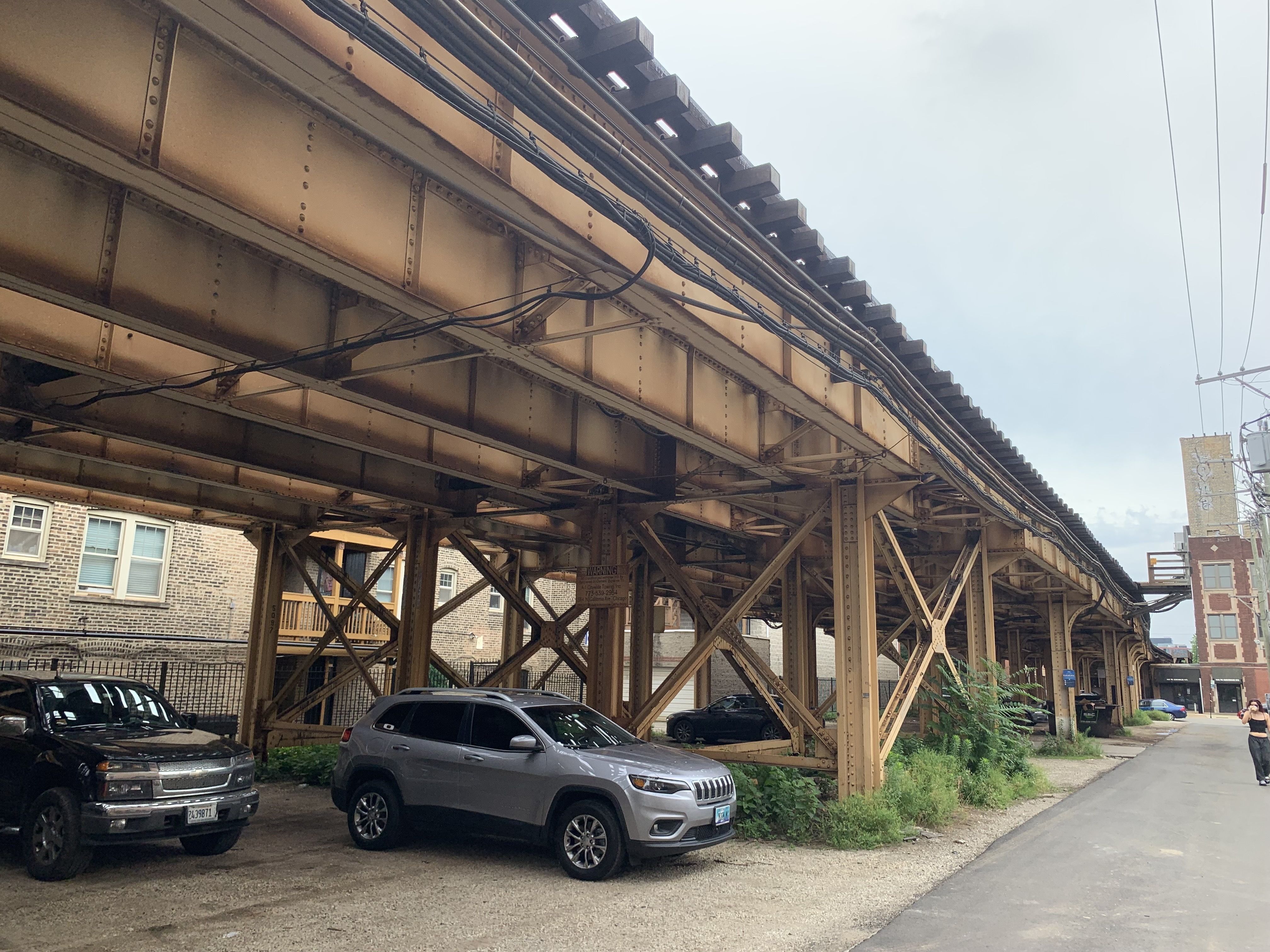 Cars under brown train tracks.